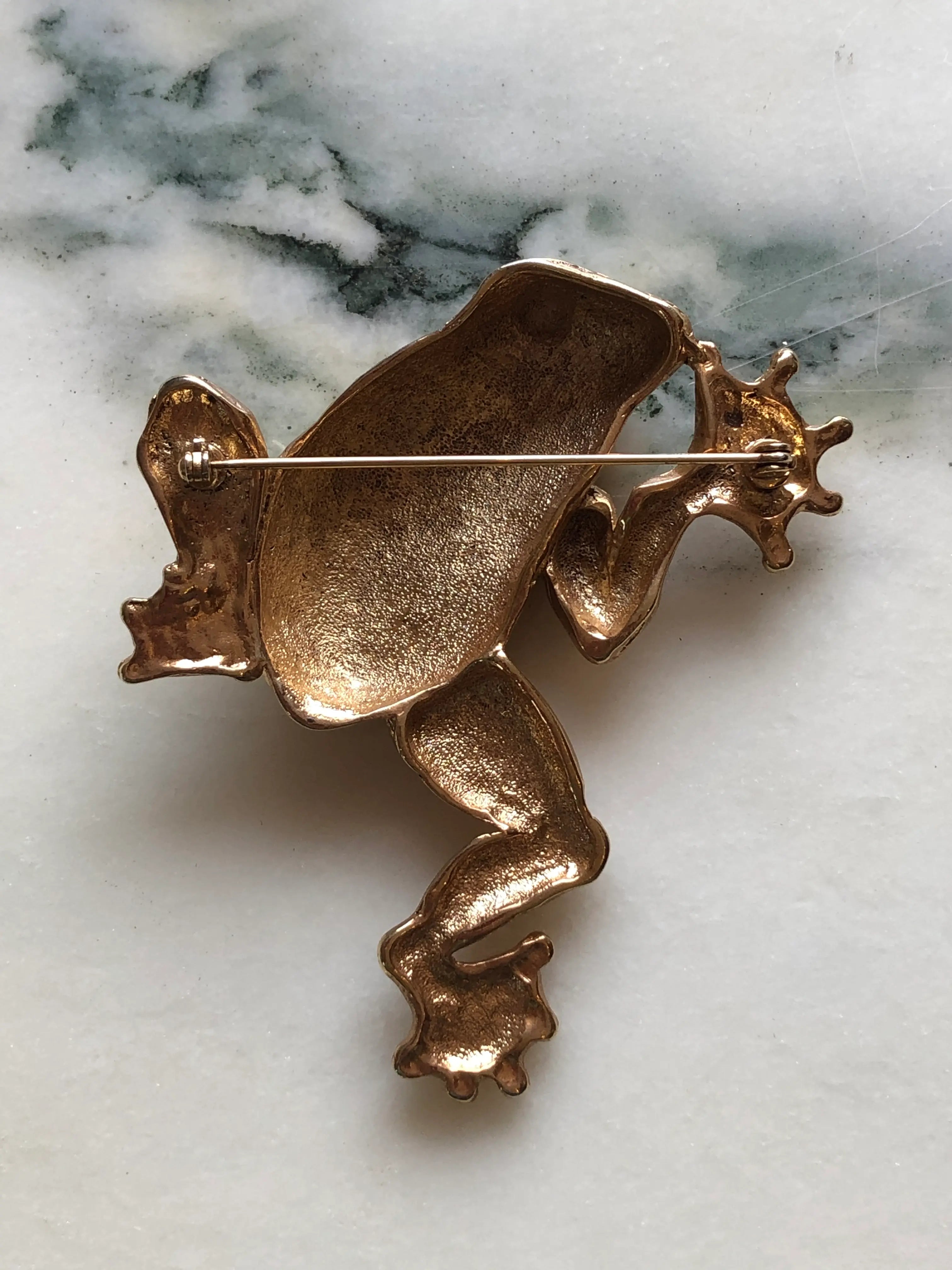 Broochella Gilded Frog vintage gold-tone statement brooch with a sculptural body, expressive eyes and detailed webbed feet, measuring approximately 8.5 × 7 cm. Photographed on white and grey marble.