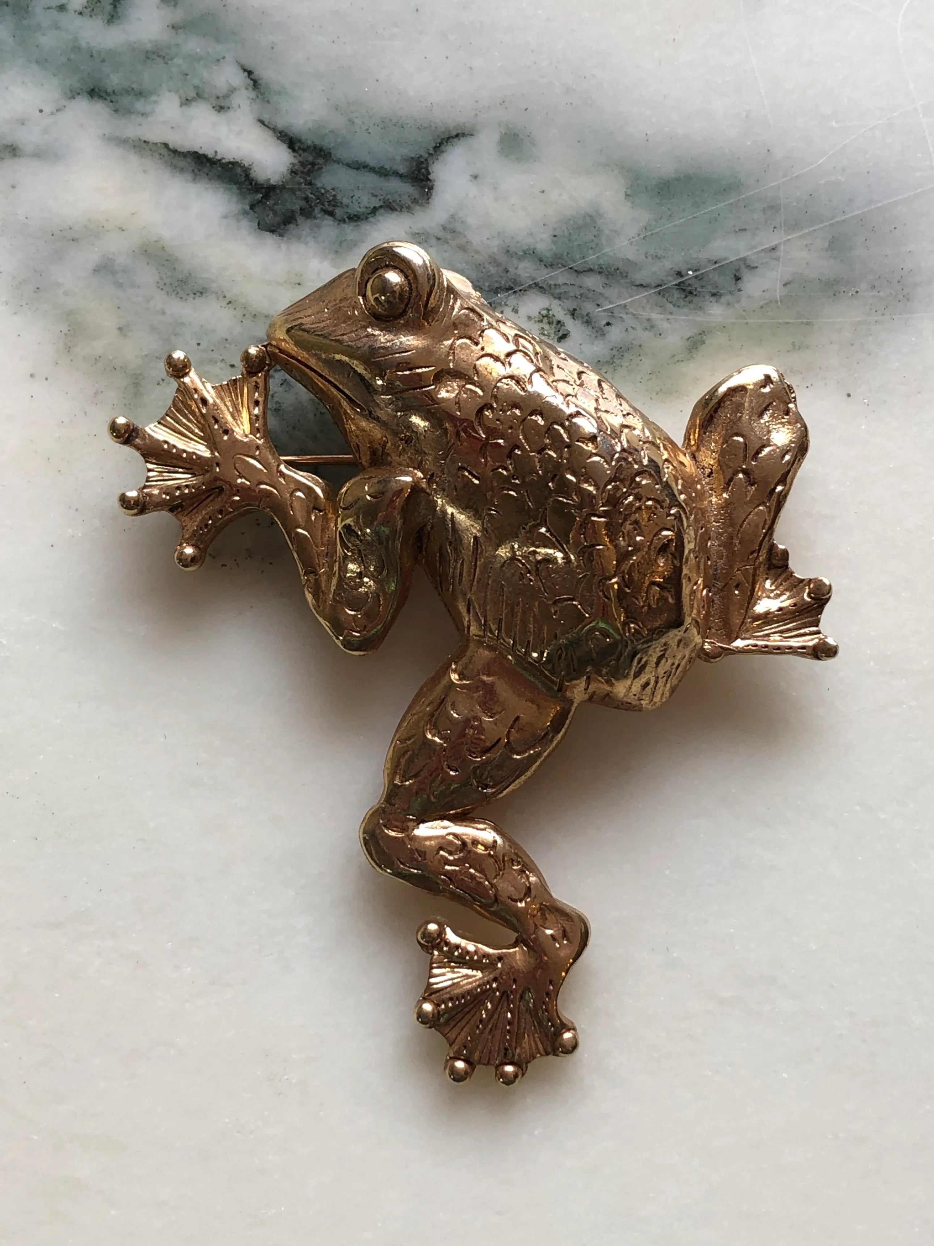Broochella Gilded Frog vintage gold-tone statement brooch with a sculptural body, expressive eyes and detailed webbed feet, measuring approximately 8.5 × 7 cm. Photographed on white and grey marble.