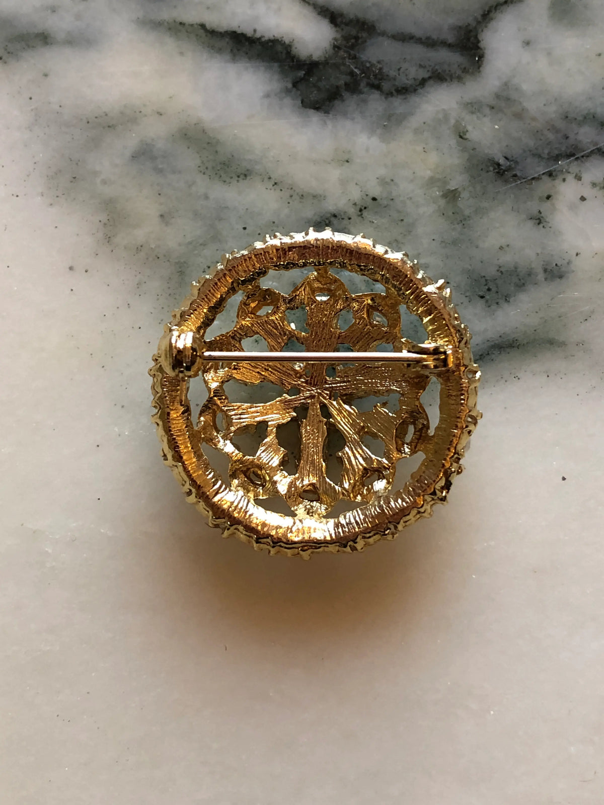 The back view of Broochella Ginevra Vintage Turquoise & Pearl Brooch featuring turquoise-blue cabochons, faux pearls and ornate gold-tone openwork on a cream and grey marble background.