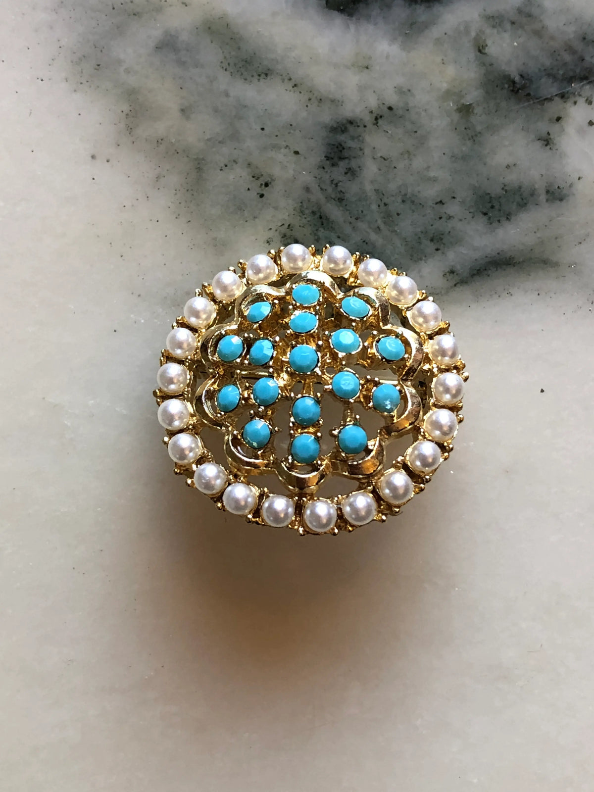 Broochella Ginevra Vintage Turquoise & Pearl Brooch featuring turquoise-blue cabochons, faux pearls and ornate gold-tone openwork on a cream and grey marble background.