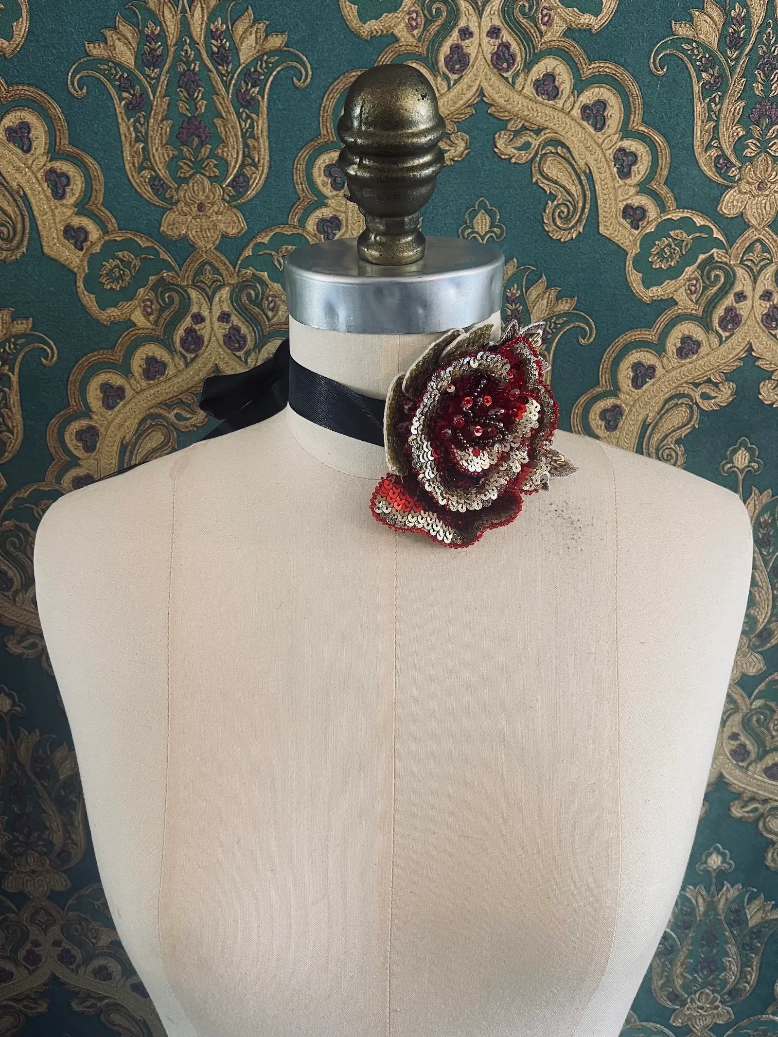 Broochella girocollo red and gold hand beaded and sequin flower chocker and brooch. Pictured on a mannequin. The background is green and gold damask wallpaper