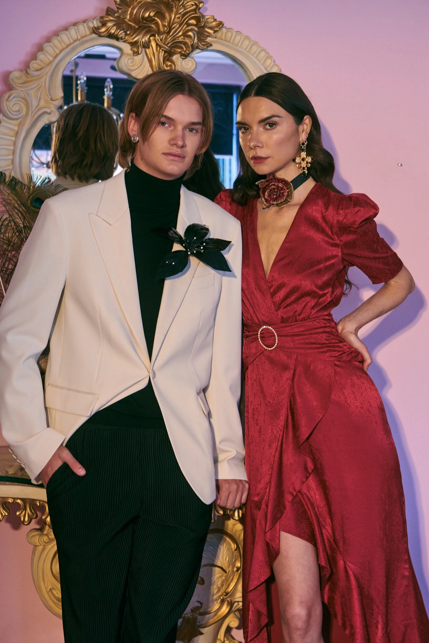 Male and femal model in red dress and white dinner jacket. She is wearing the broochella girocollo choker around her neck. The background is pink