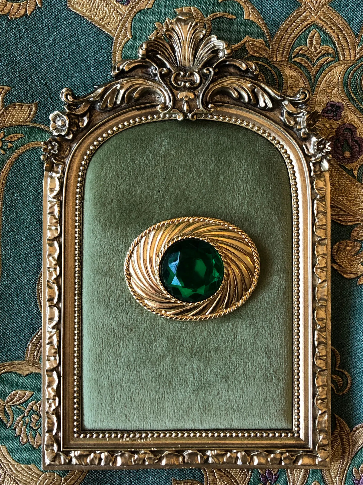 Broochella Giulia vintage Ungaro designer brooch showing the gold-tone reverse with embossed Ungaro Paris signature, textured metal finish and traditional pin fastening, photographed on a cream marble background with subtle beige veining.
