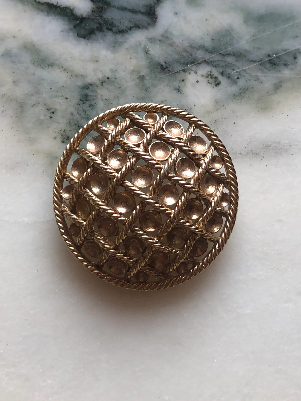 Broochella Golden Constellation vintage round brooch with raised gold-tone discs and an intricate twisted rope lattice, measuring approximately 4 cm across. Photographed on white and grey marble