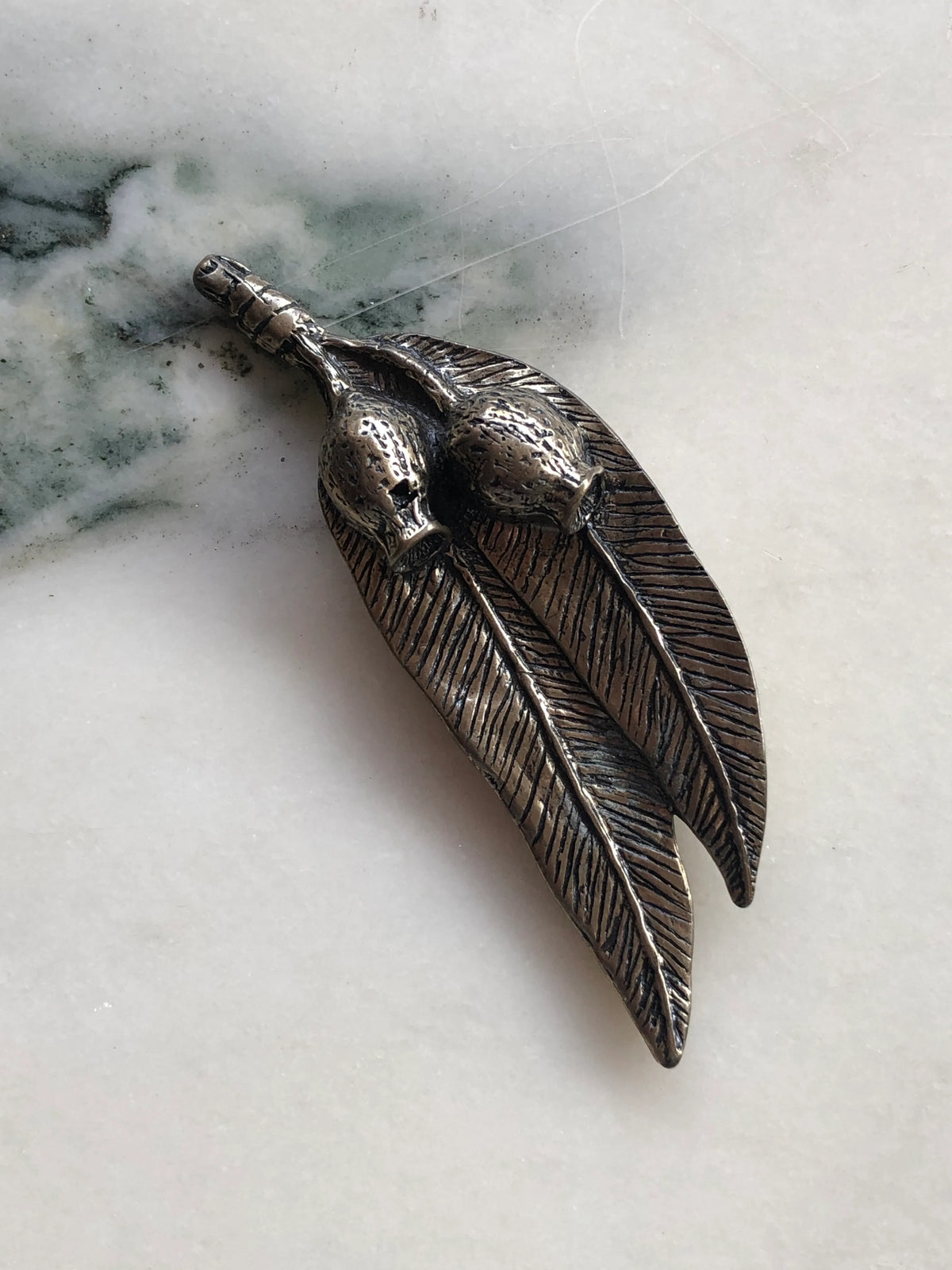 Broochella Golden Gumnut Trail Vintage Brooch with sculpted gumnuts and textured eucalyptus leaves in antiqued bronze-tone metal, photographed on white marble with natural grey-green veining.
