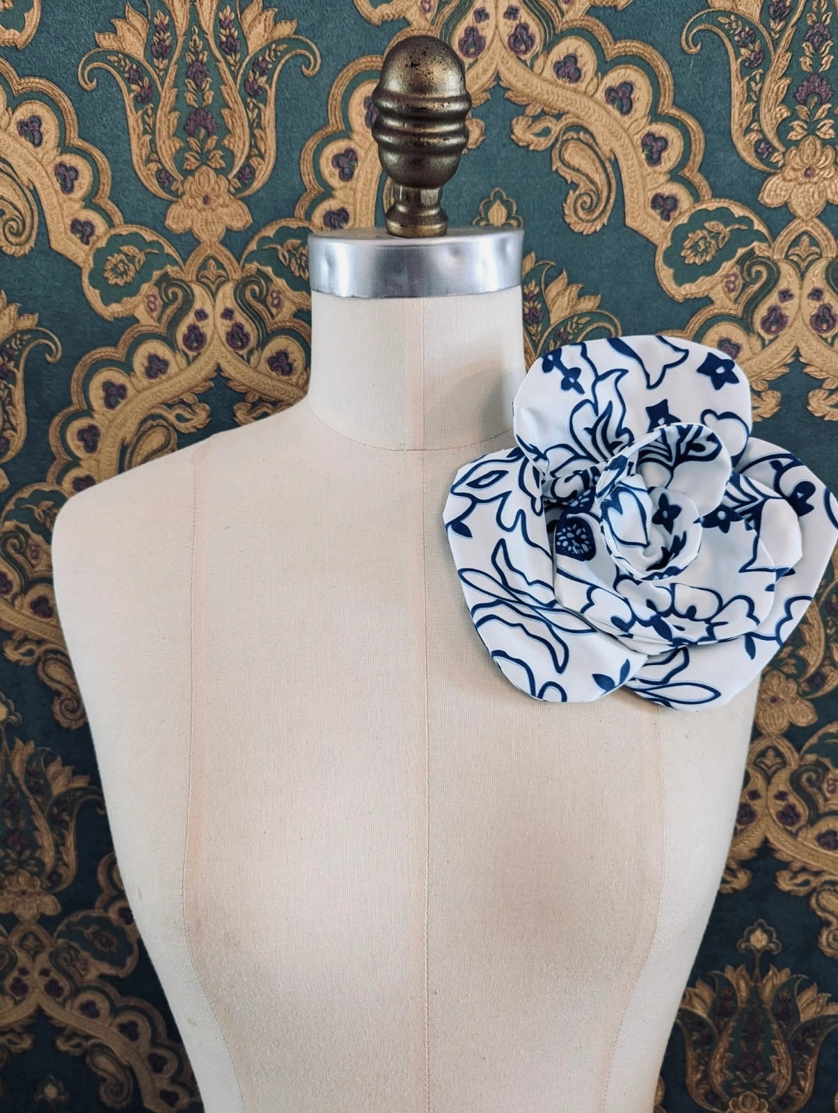 Broochella electra flower choker and brooch with blue and white floral print.  Pictured on a mannequin.  The background is green and gold damask wallpaper.