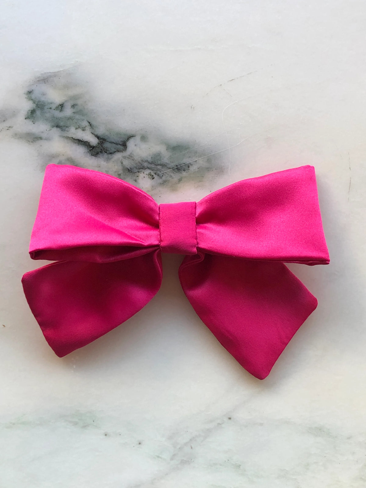 Broochella The Hollywood Satin Bow Brooch in vibrant pink satin, photographed on a white marble background.