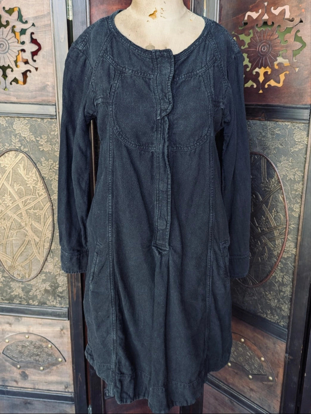 A Broochella Isable Marant Etoile black long-sleeve tunic dress displayed on a mannequin torso, set against a decorative wooden screen with intricate carvings.