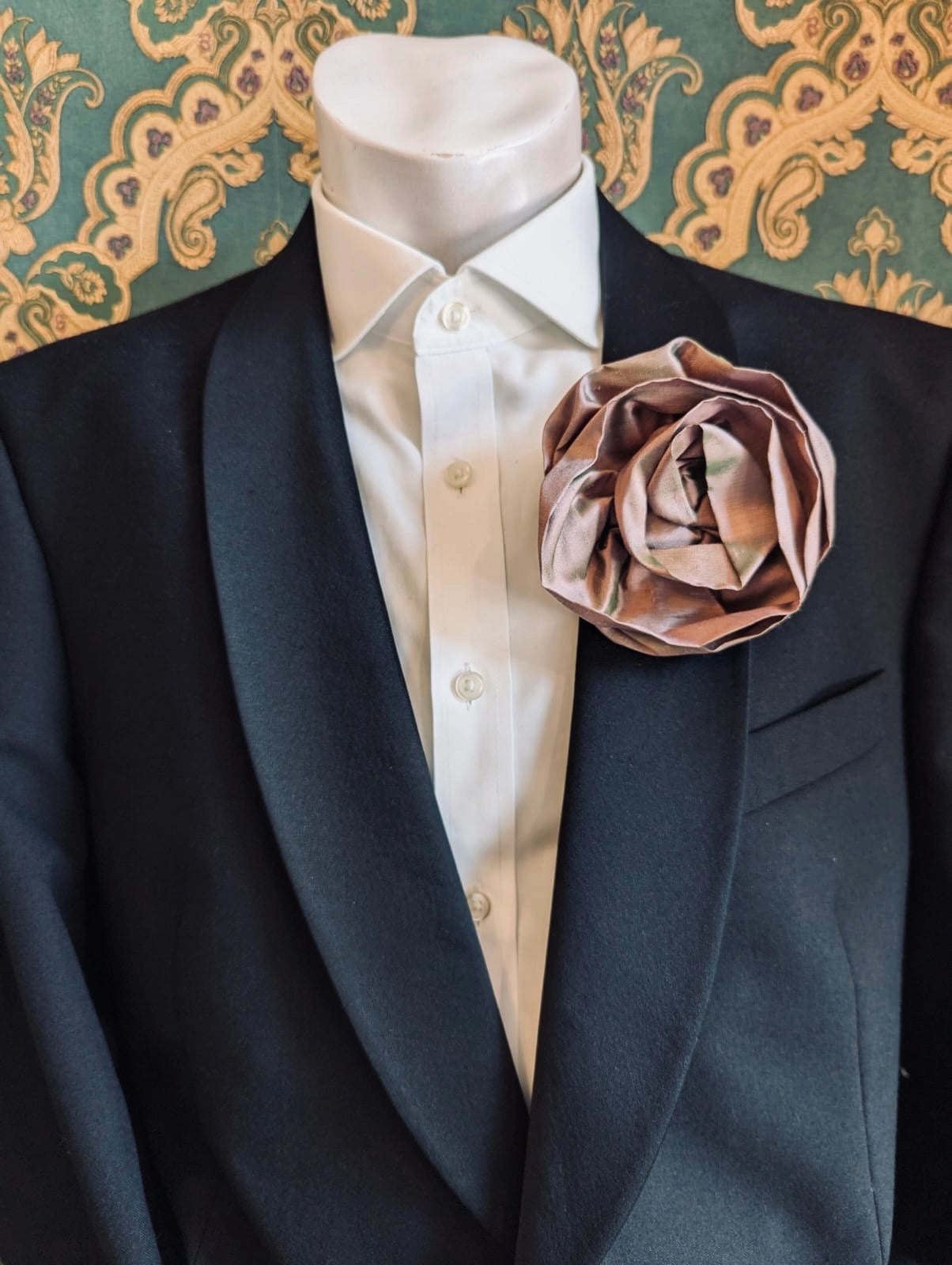 Broochella Isabella Rossellini handmade silk rosette flower brooch in blush pink. Pictured on a mannequin.  The background is green and gold damask wallpaper