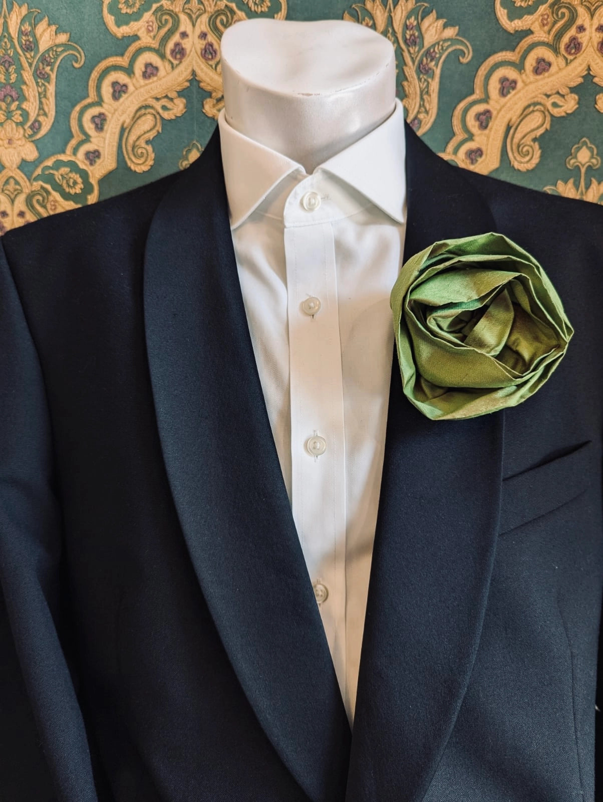 Broochella Isabella Rossellini handmade silk rosette flower brooch in green. Pictured on a mannequin.  The background is green and gold damask wallpaper