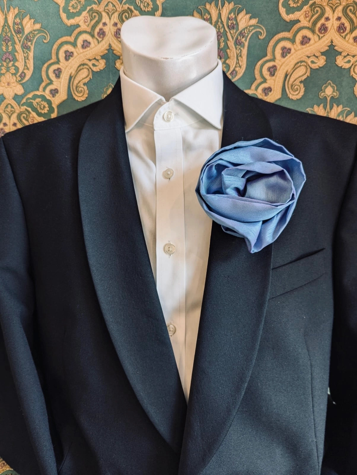Broochella Isabella Rossellini handmade silk rosette flower brooch in powder blue. Pictured on a mannequin.  The background is green and gold damask wallpaper