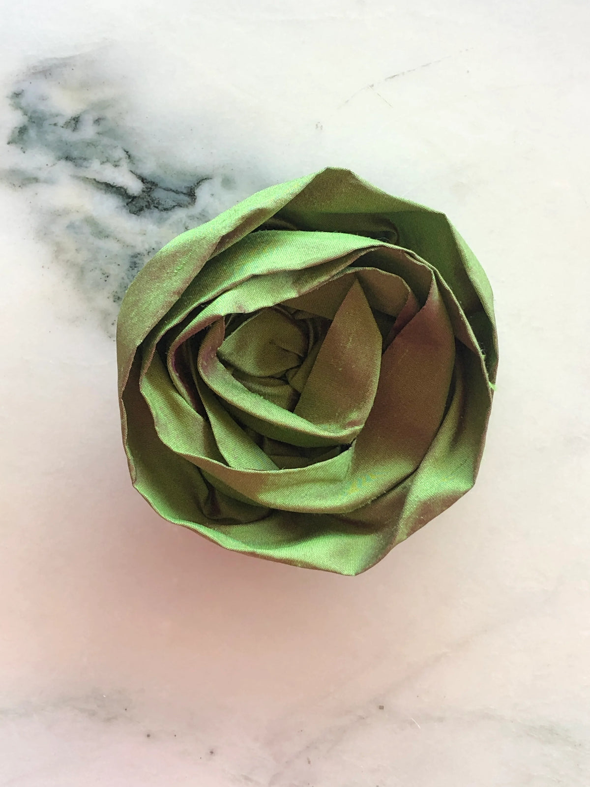 Handmade Broochella Isabella Rossellini silk rosette brooch in green, a sculptural designer flower brooch with individually shaped fabric petals, photographed on white marble.