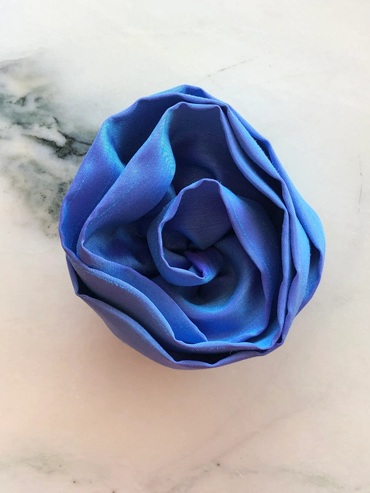 Handmade Broochella Isabella Rossellini designer silk rosette brooch for men in powder blue, a sophisticated flower lapel accessory for suits and jackets, photographed on white marble.