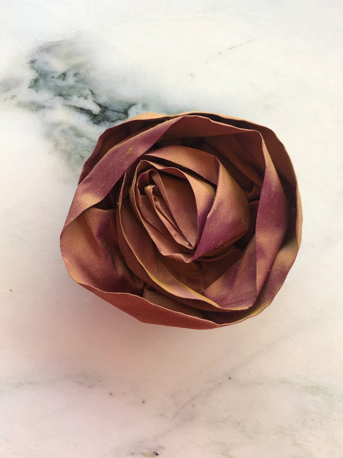 Handmade Broochella Isabella Rossellini designer silk rosette brooch in warm rust, with softly sculpted layered petals creating an oversized fabric rose, photographed on white marble.