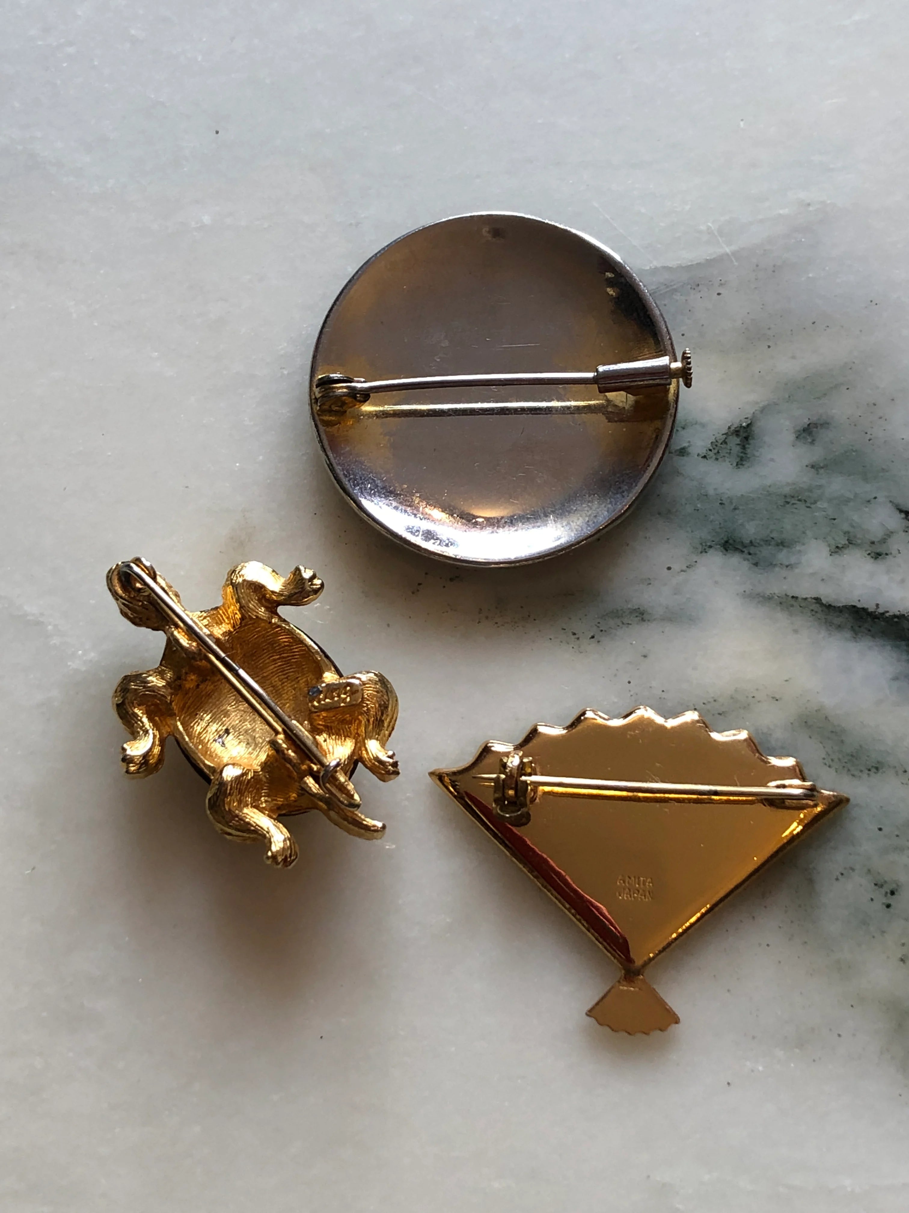 The back view Broochella Kyoto Noir vintage black and gold brooch trio featuring an Amita Japan fan, floral medallion and decorative turtle. The background is white marble.