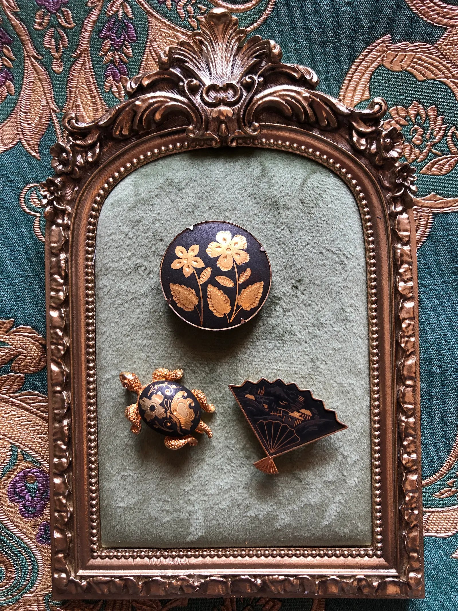 Broochella Kyoto Noir vintage black and gold brooch trio featuring an Amita Japan fan, floral medallion and decorative turtle.  All set against a textured sage green velvet background.