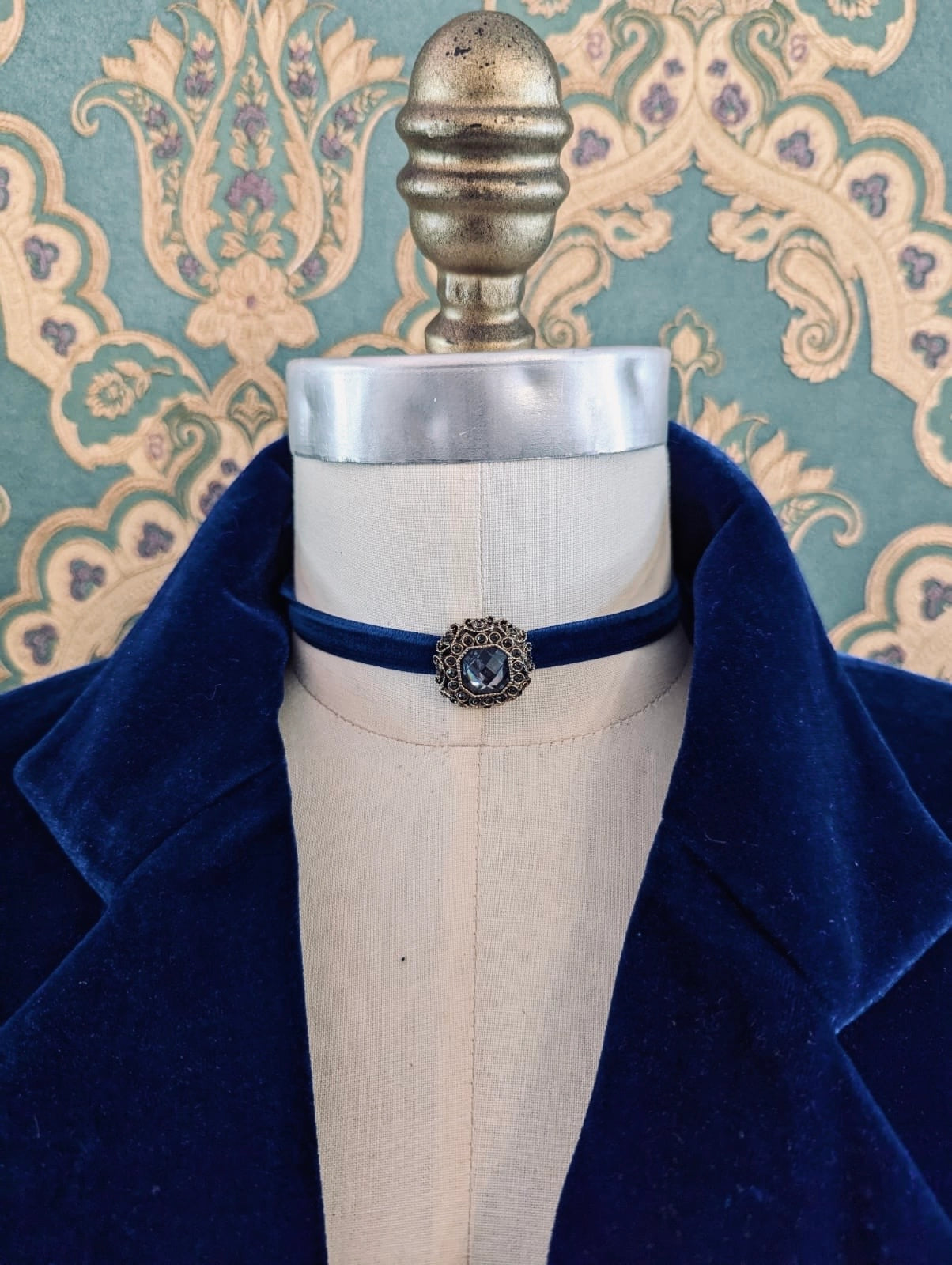 Broochella blue lady whistledown velvet choker with crystal embellishment.  Pictured on a mannequin.  The background is green and gold damask wallpaper