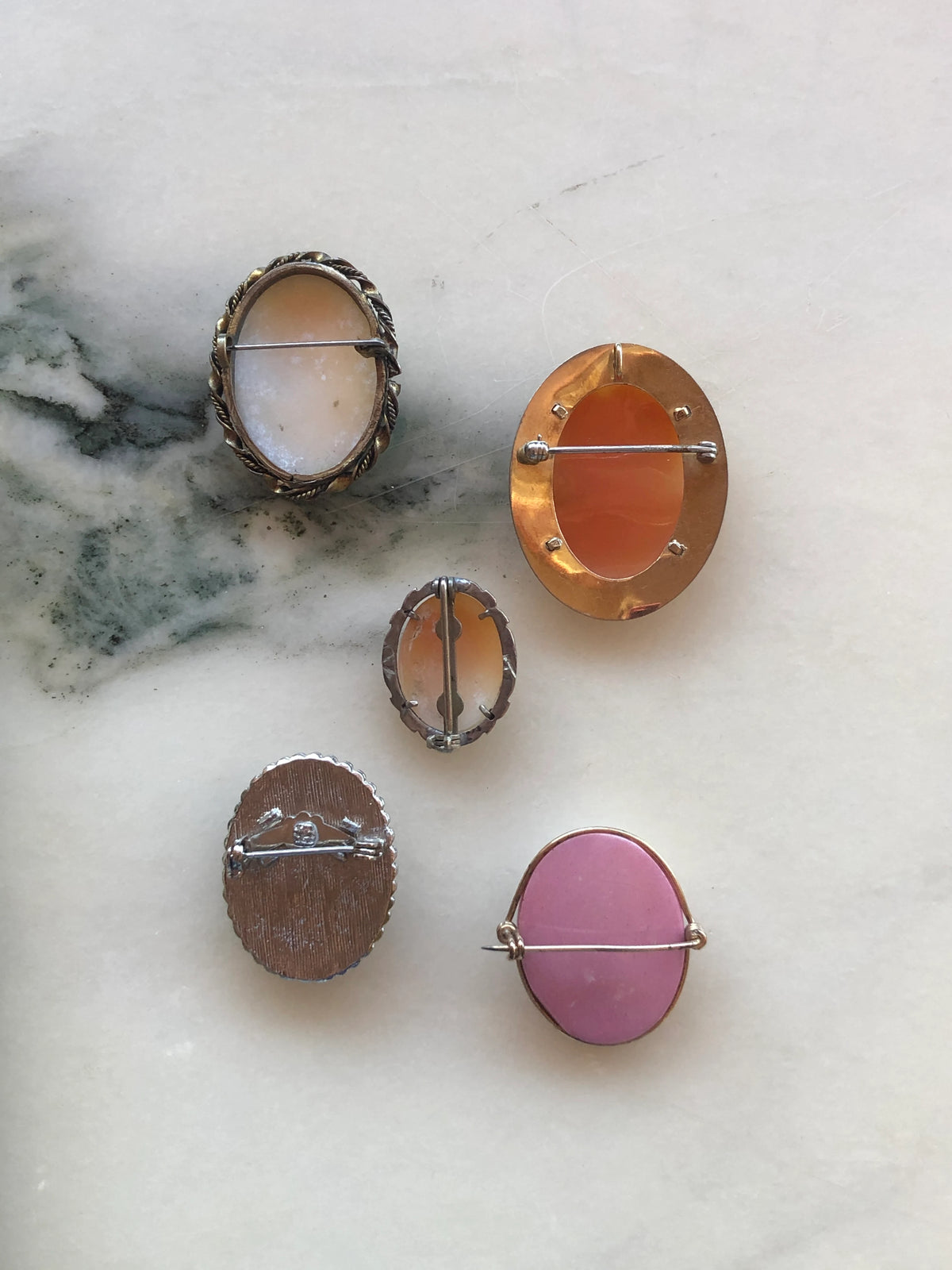 The back view of Broochella le camee set of five vintage cameo brooches. The background is white marble