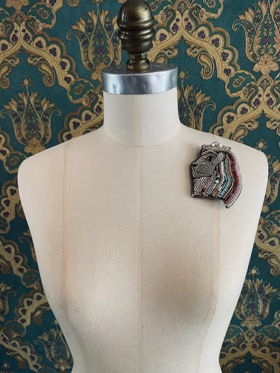 Broochella leo zodiac hand beaded figural designer brooch. The background is green and gold damask wallpaper
