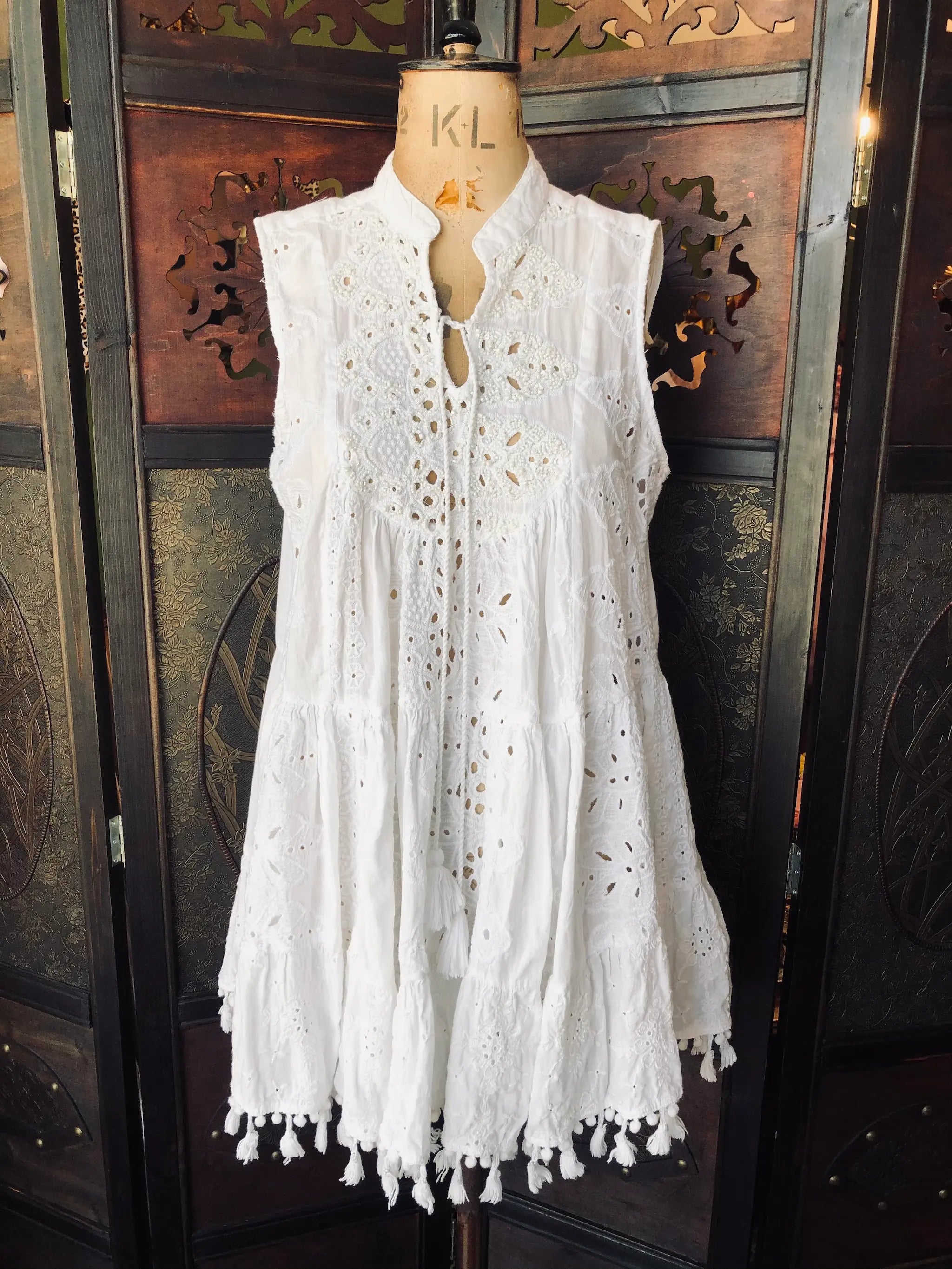 Broochella Leoni al Sole by Giacomo Cinque White lace dress on a mannequin against a decorative wooden background