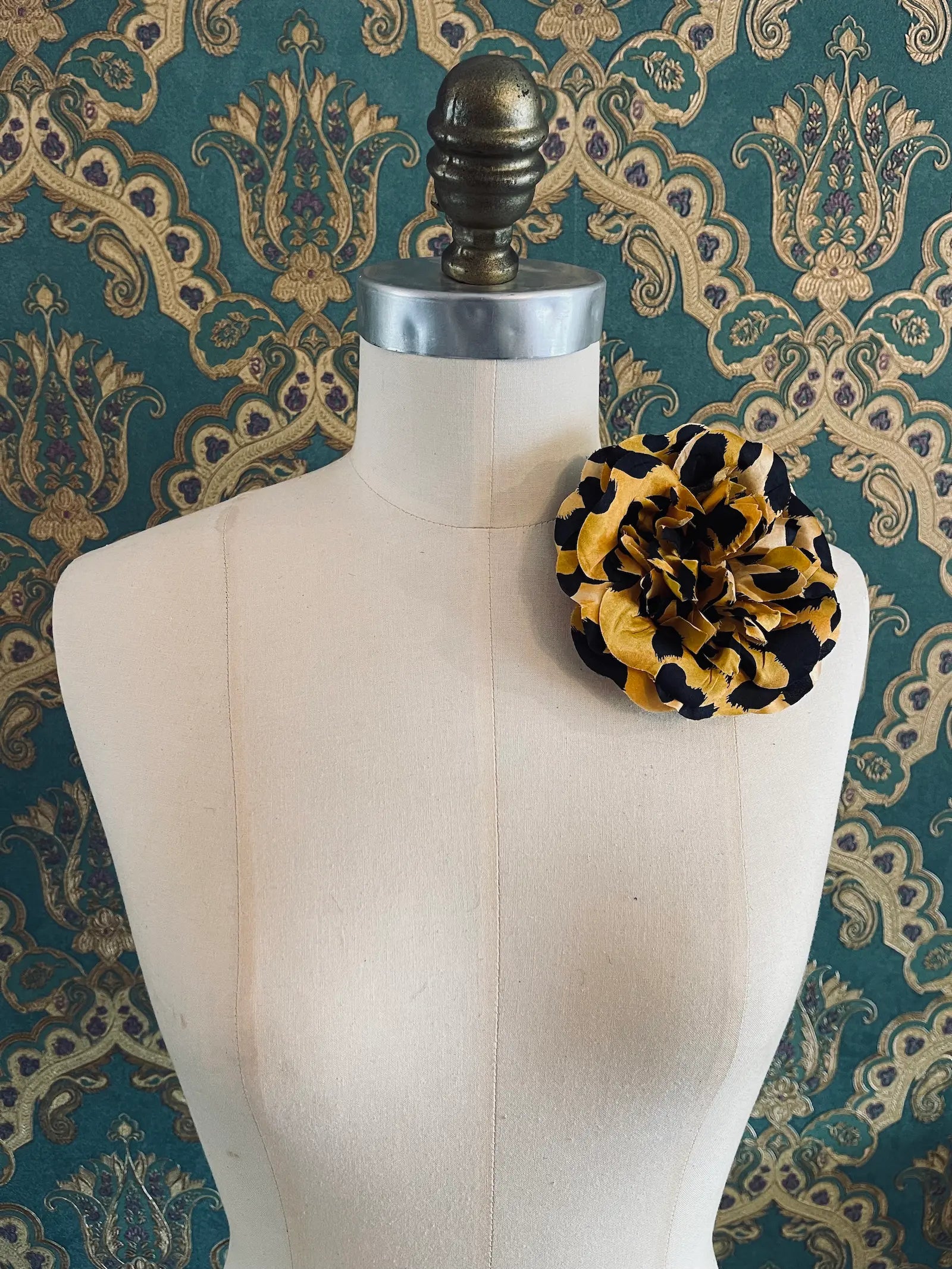Broochella leopard handmade desginer fabric flower brooch. Styled on a mannequin. The background is green and gold damask wallpaper