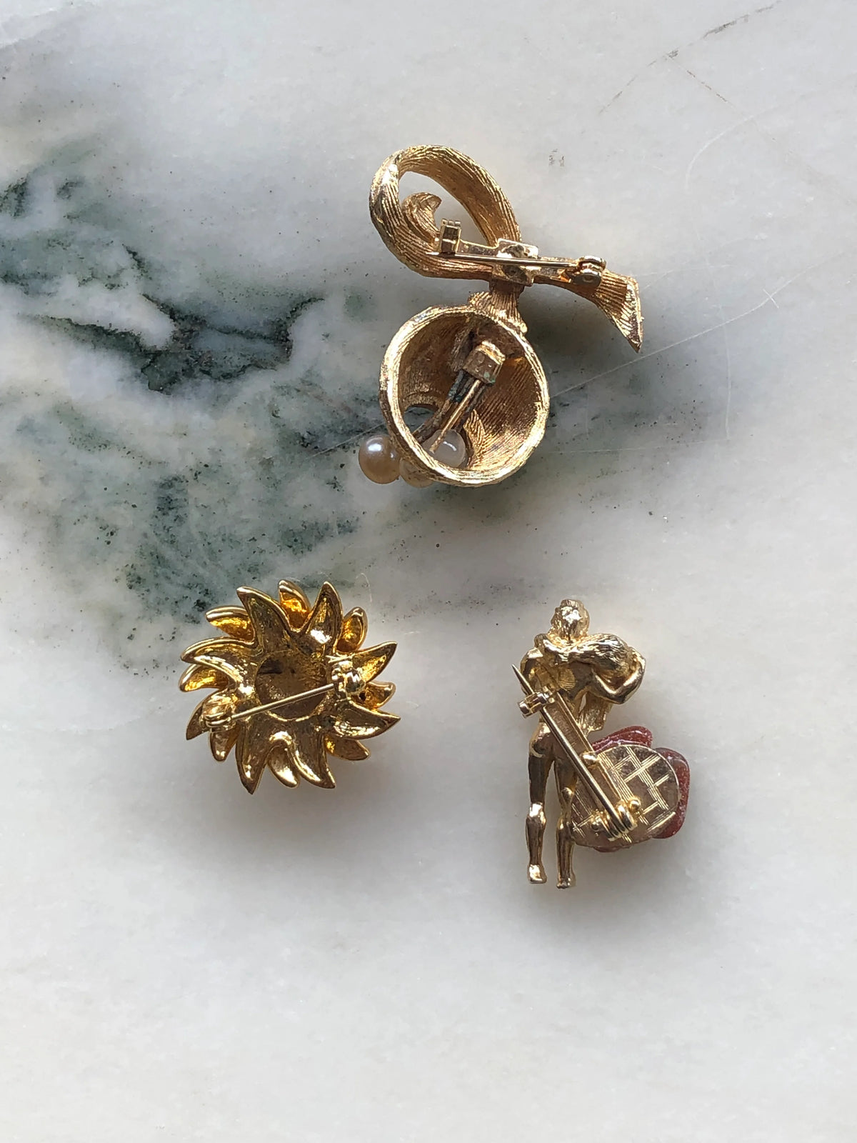 Broochella Les Petites Curiosités Vintage Brooch Trio back view showing the gold-tone settings and individual pin fastenings of all three brooches, photographed on a white marble background with soft grey-green veining.