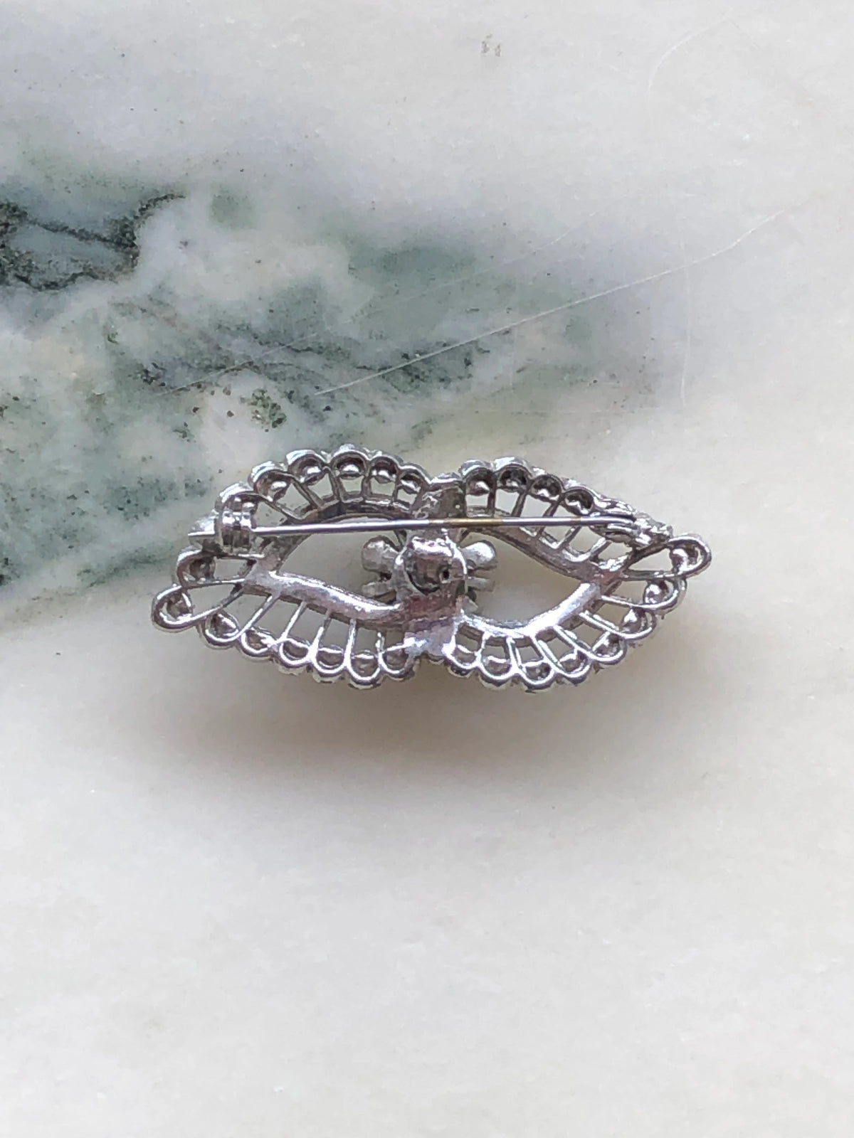 Broochella Luciana Vintage Silver Filigree Crystal Brooch showing the reverse of its ornate openwork metal setting and traditional horizontal pin fastening, photographed on white marble with natural grey veining.