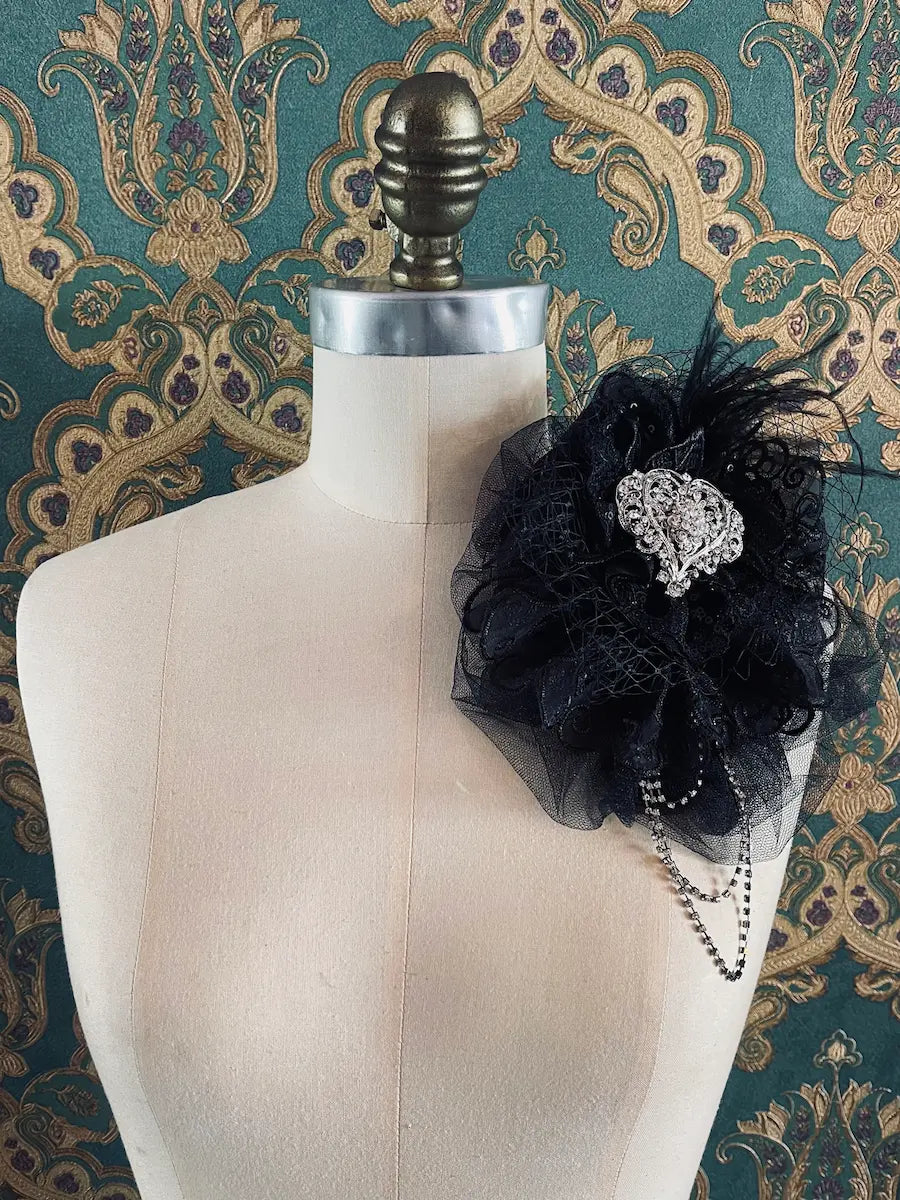 Broochella Madonna black lace embellished handmade designer brooch. Pictured on a mannequin. The background is green and gold damask wallpaper