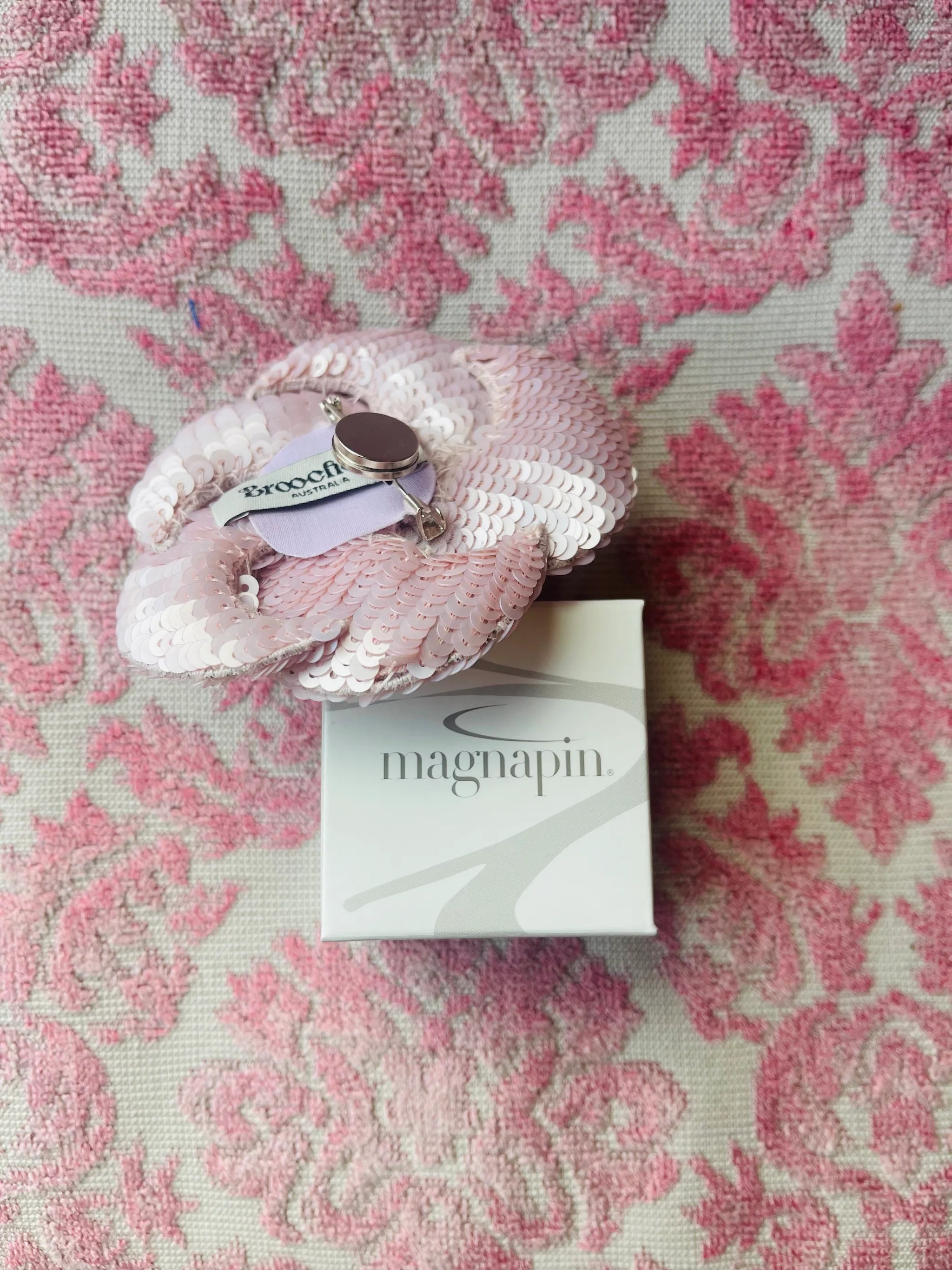 Broochella magnapin magnet attached to a pink flower brooch.  On pink damask background