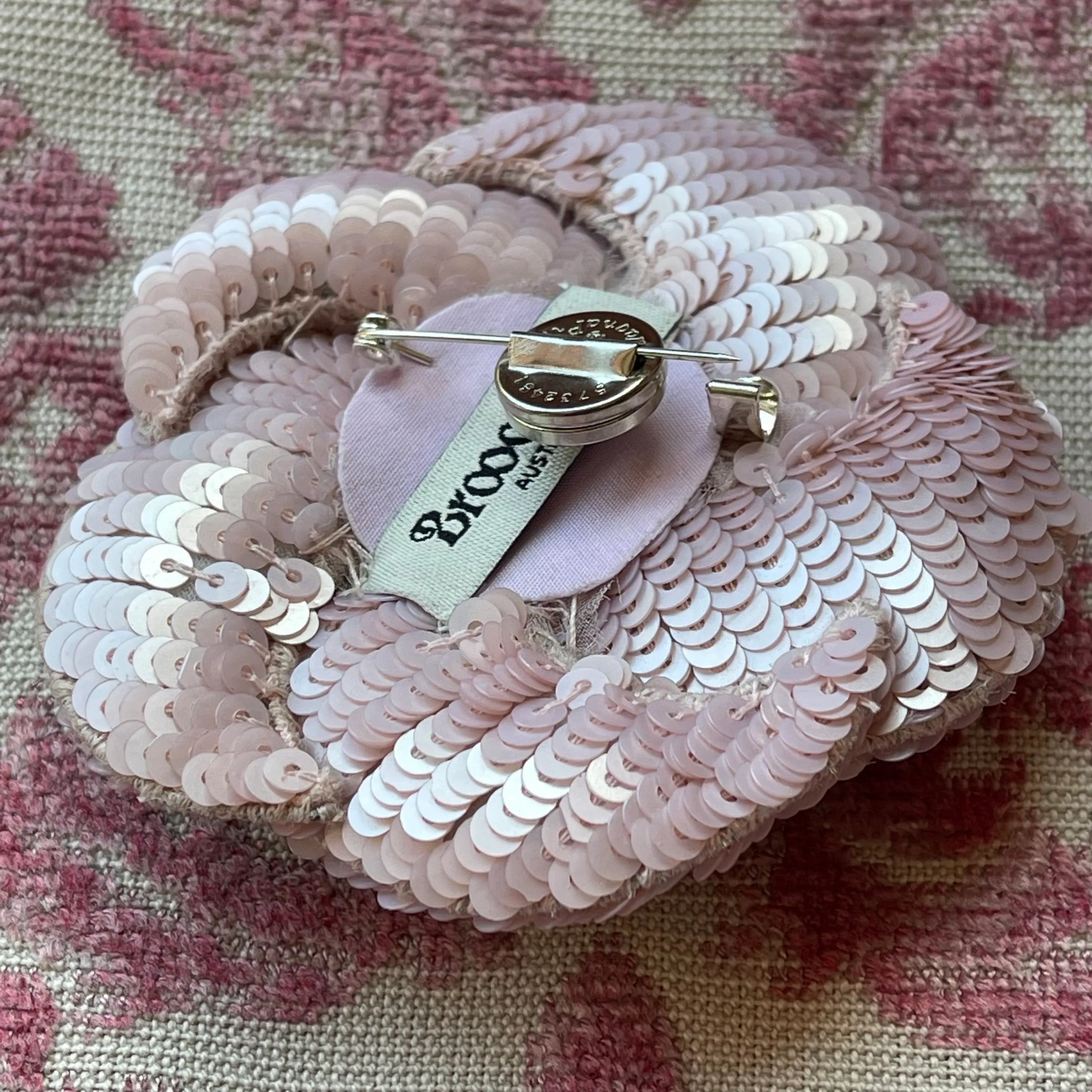 Broochella magna pin magnet attached to a pink flower brooch. The background is pink damask fabric