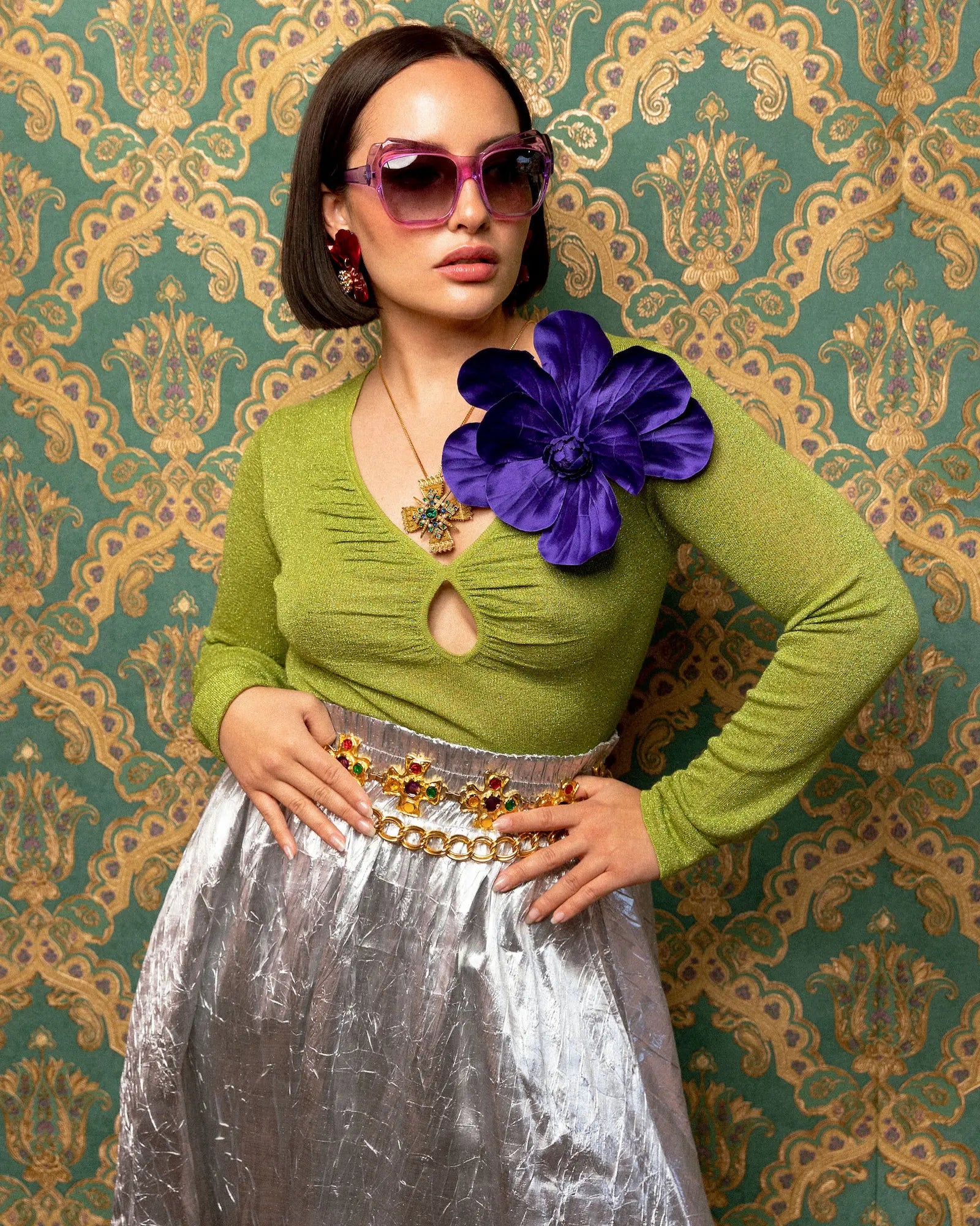 Woman wearing a green top with a purple Broochella magnolia flower brooch against a patterned wall