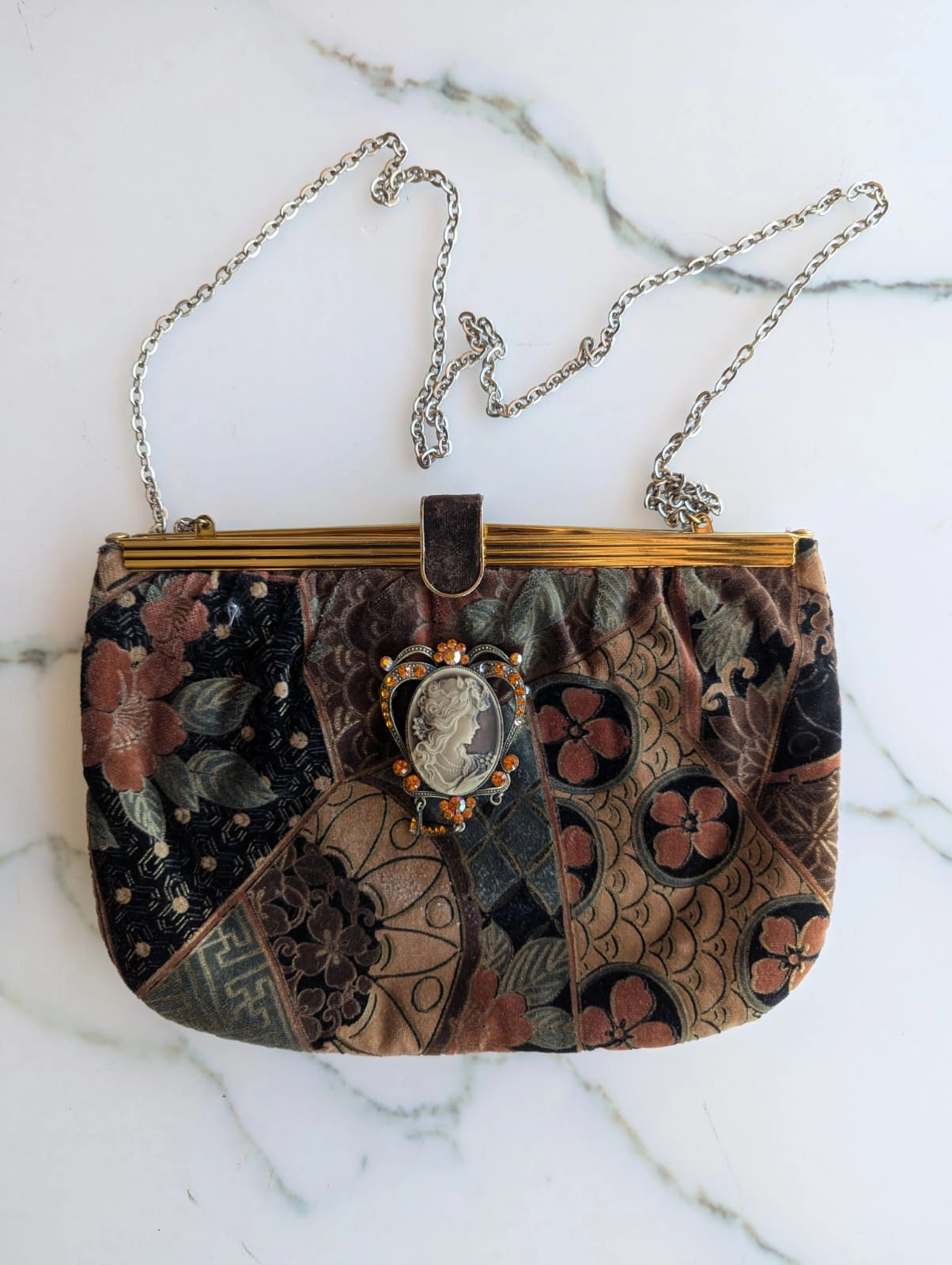 Broochella Maison Broche la cameo du jardin vintage, velvet, patterned handbag in shades of beige, blue and pink. There is a vintage cameo pinned to the bag. The background is white marble