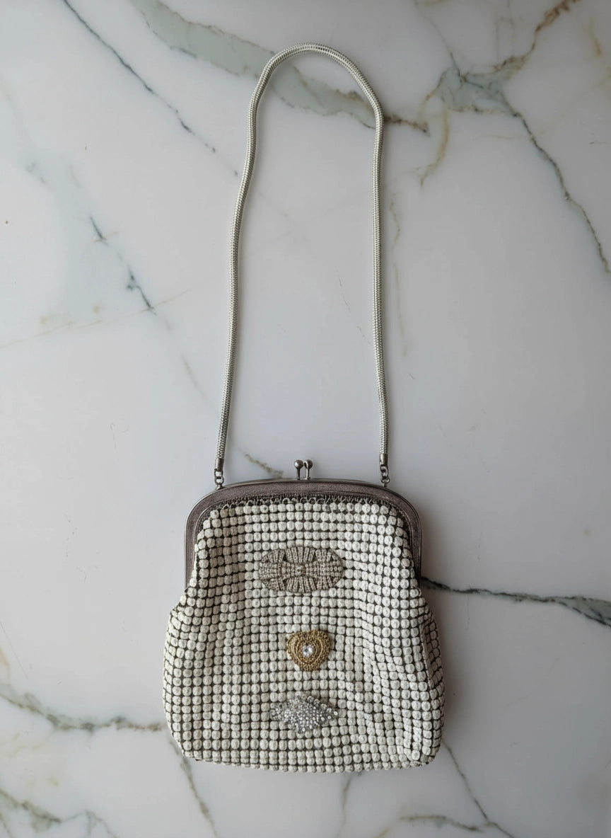 Broochella Maison Broche le bijou du soir vintage white glomesh bag, with vintage brooch embellishments. The background is white marble.