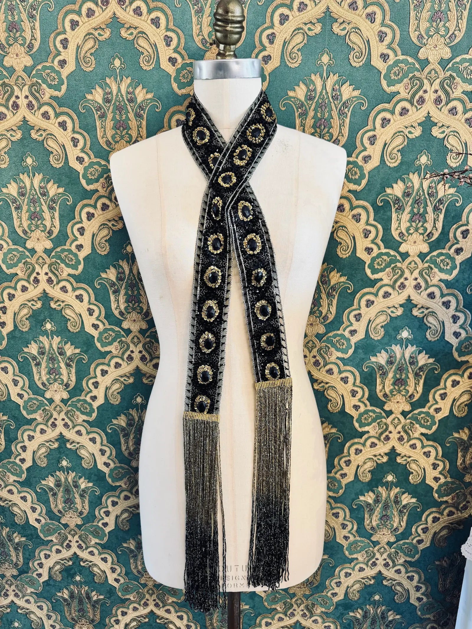 Broochella Antionette handmade fringe black and gold embellished foulard neck tie. Pictured on a mannequin. The background is green and gold damask wallpaper.