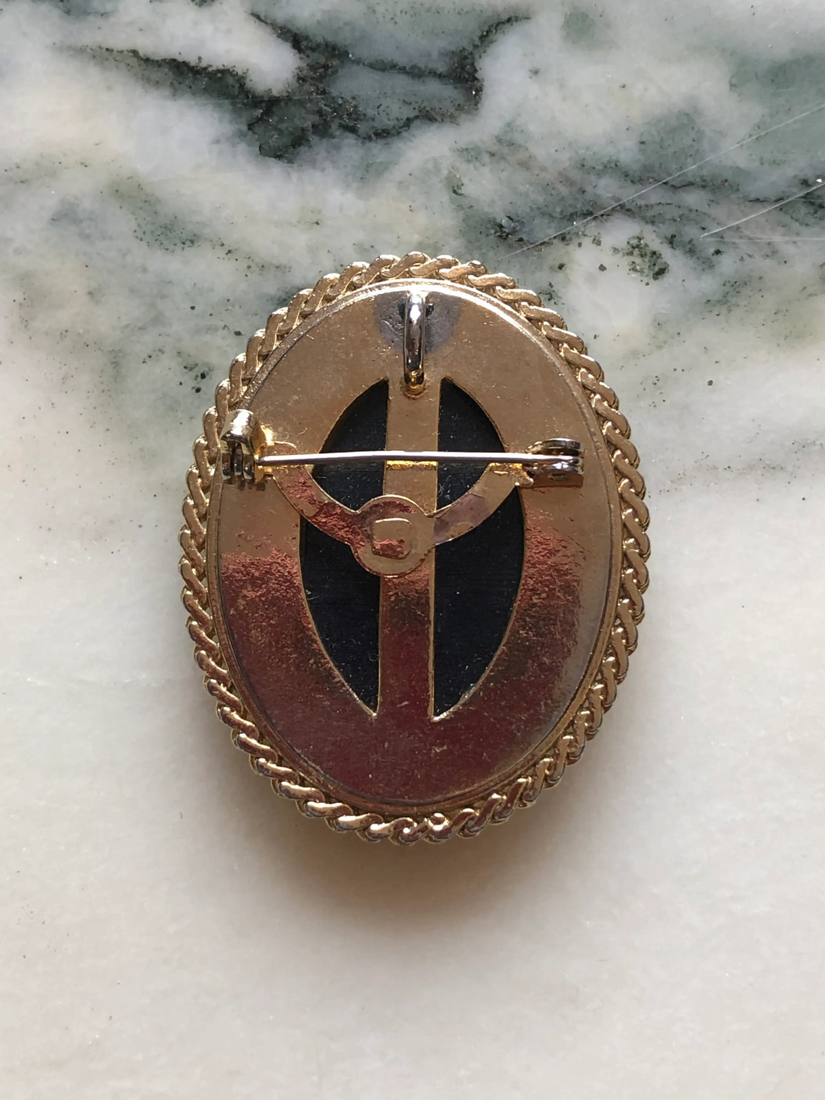 The back view Broochella Marigold Garden vintage oval brooch with orange and amber flowers on a black background, a glossy domed centre and textured gold-tone frame, measuring approximately 4.5 × 3.5 cm. Pictured on white and grey marble