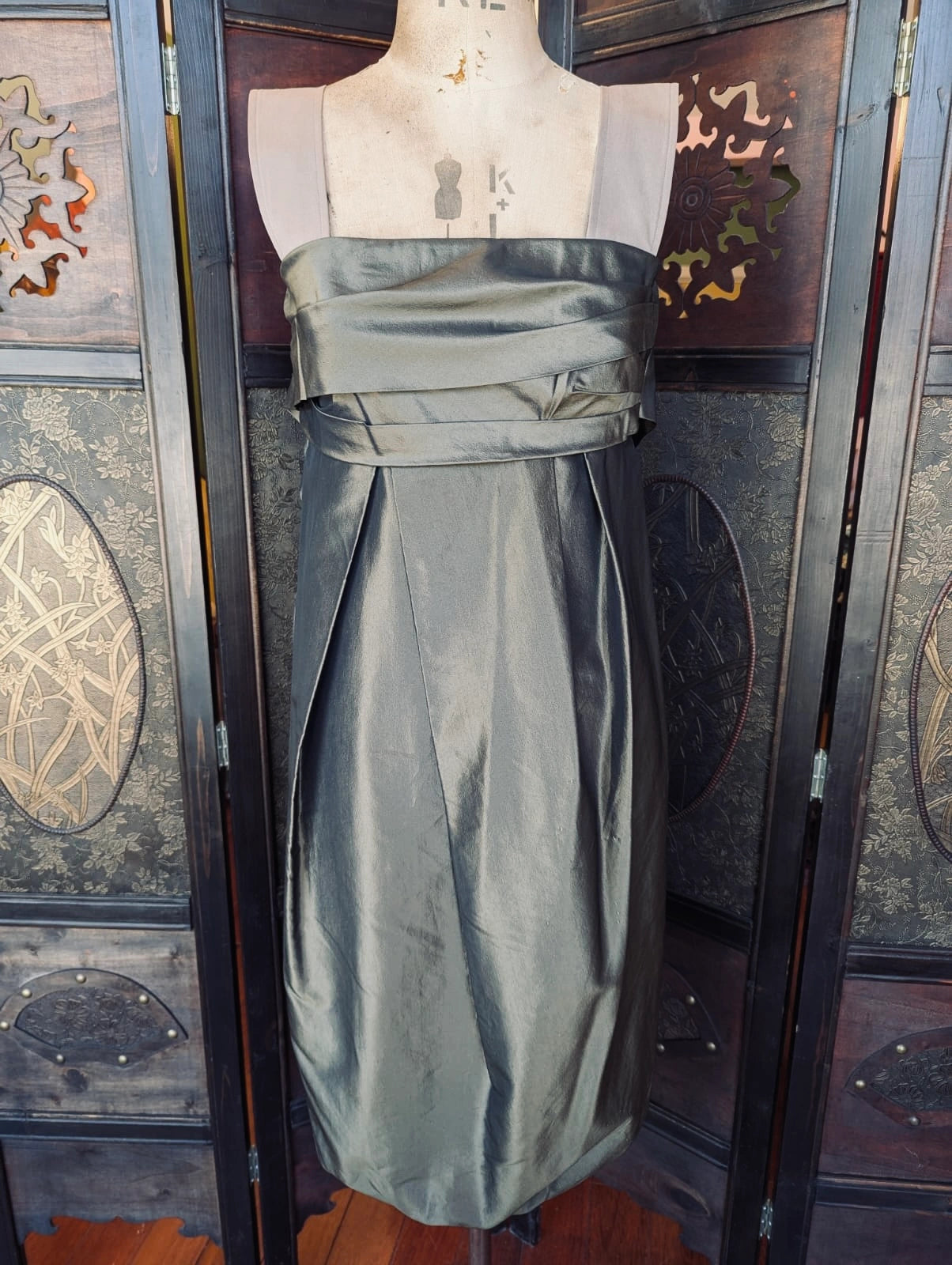 Broochella Max Mara Olive Green Cocktail midi dress with taffeta body and thick beige straps. It is pictured on a mannequin. The background is an ornate dark wood room divider.