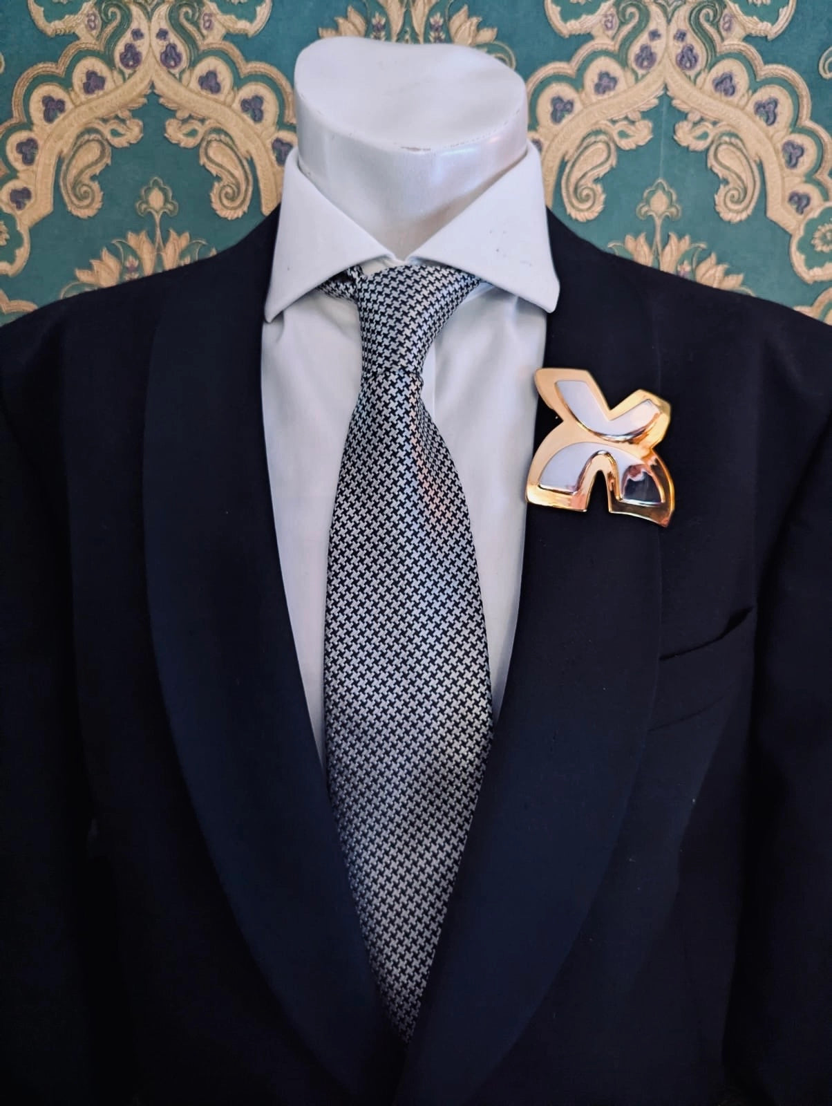 Broochella men's brooches with meaning freedom gold metal and silver brooch. Pinned to a men's mannequin wearing a black suit and houndstooth tie. The background is green and gold damask wallpaper.