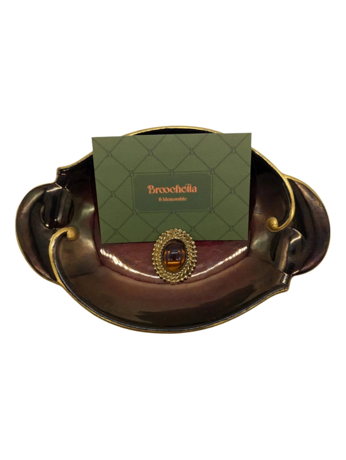 Broochella vintage amber crest tie clip. The centre is a amber stone, the outer is gold metal. The pin is pictured on a burgundy and gold wembley ware tray. There is a broochella green card behind the pin. The background is white