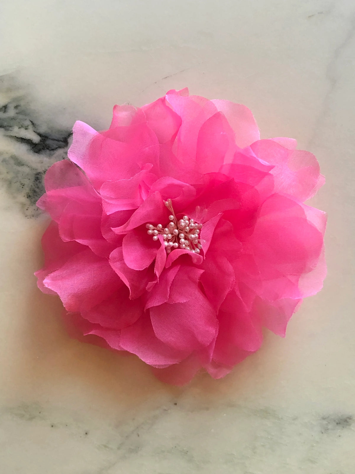 Broochella men’s Aubrieta handmade designer flower brooch in vivid pink fabric with pearl stamen detailing, photographed on a white and green veined marble background.