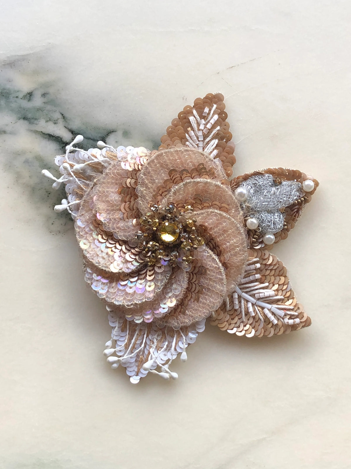 Broochella Men’s Blossom de Luxe Sequin Brooch featuring a dimensional champagne sequin flower with beaded leaves, pearl details and crystal embellishments, photographed on a white marble background.