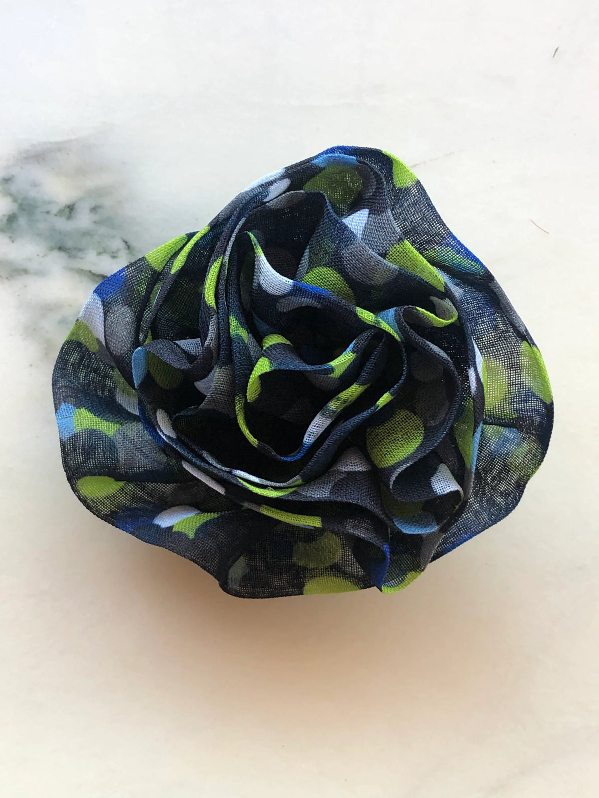 Broochella Men’s Brassica Flower Brooch in navy, a handmade designer fabric flower with sculptural layered petals and blue, green and white print, photographed on white marble.