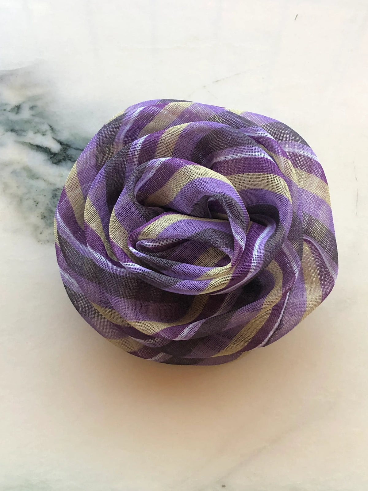 Broochella Men’s Brassica Flower Brooch in purple, a handmade designer fabric flower with sculptural layered petals and purple, cream and charcoal stripes, photographed on white marble.