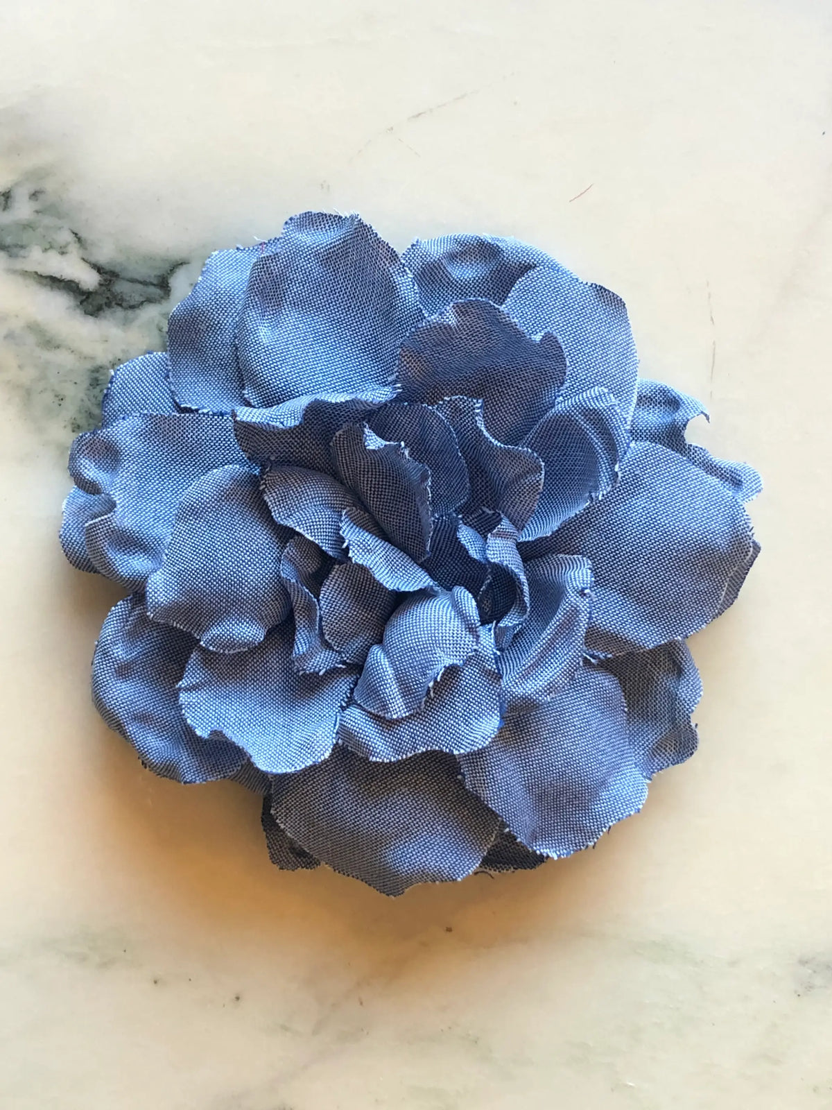 Broochella Men’s Denim Flower Brooch in navy, a handmade designer statement flower with sculptural layered denim petals, photographed on a white marble background.