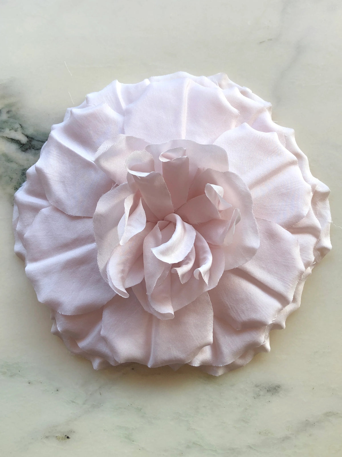 Broochella Men’s Femmina handmade designer flower brooch in soft yellow fabric, with oversized sculptural layered petals and a ruffled centre, photographed on a white marble background with natural green veining.