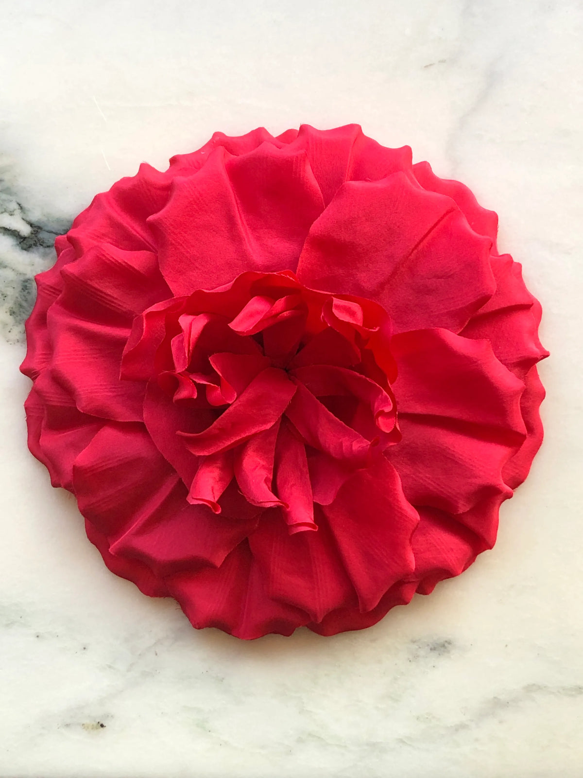 Broochella Men’s Femmina handmade designer flower brooch in vibrant red fabric, with oversized sculptural layered petals and a dramatic ruffled centre, photographed on a white marble background with natural green veining.