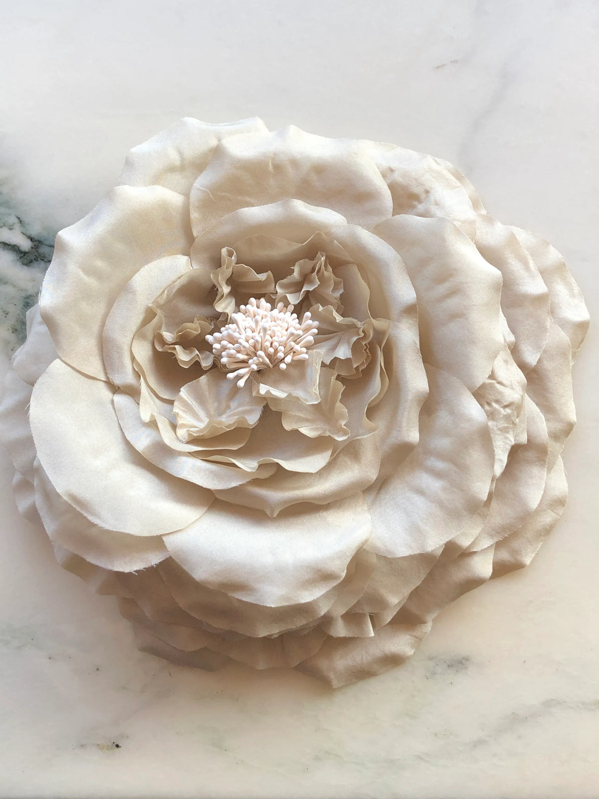 Broochella Men’s Fiorita handmade designer flower brooch in brown fabric, featuring oversized layered petals and delicate stamen detailing, photographed on a white and green veined marble background.