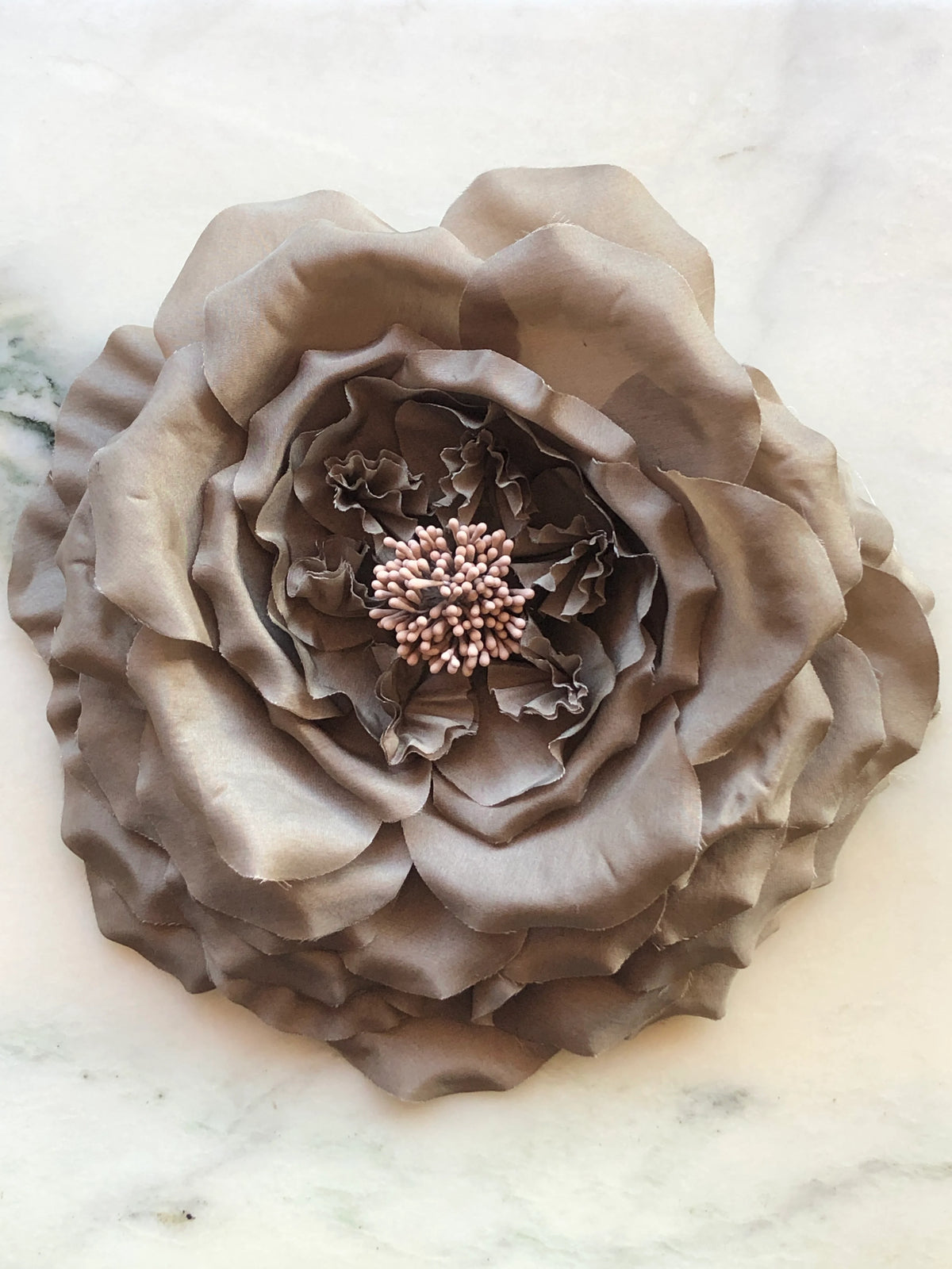 Broochella Men’s Fiorita handmade designer flower brooch in brown fabric, featuring oversized layered petals and delicate stamen detailing, photographed on a white and green veined marble background.