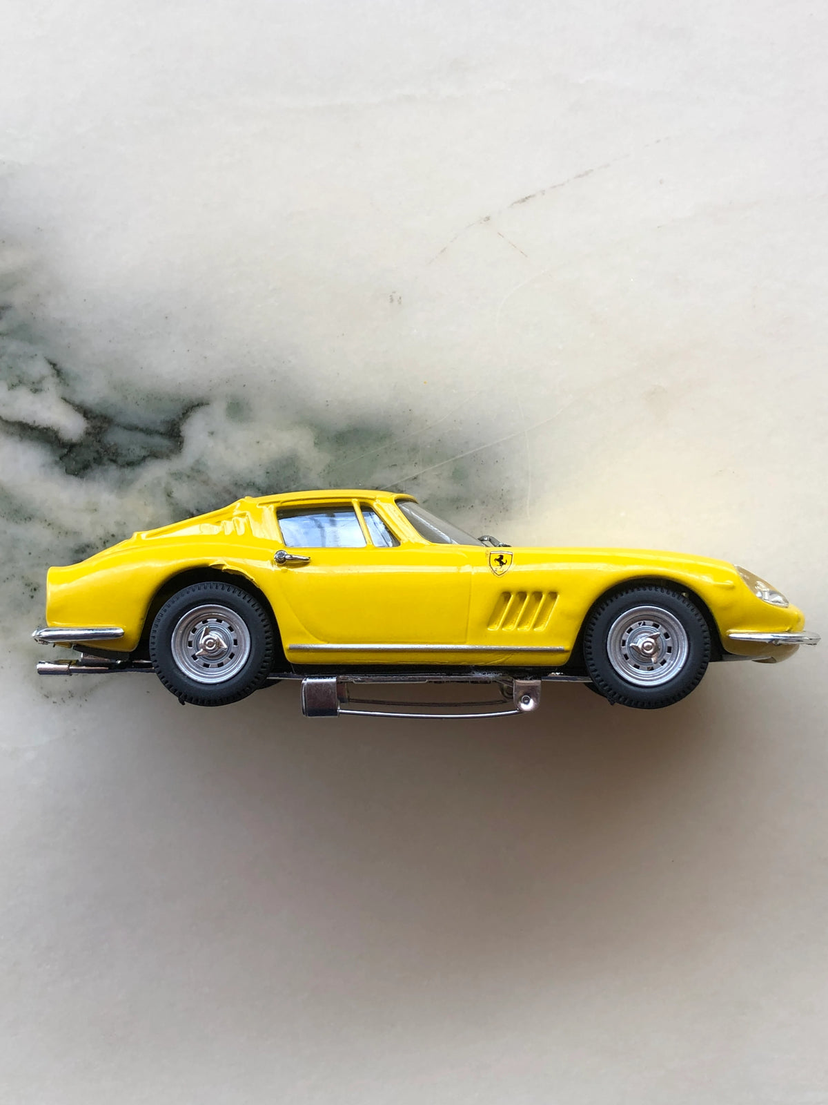 Broochella Men's Giallo Fiorano No.275 Vintage Ferrari Racing Brooch in side profile, featuring a yellow classic Ferrari coupe with chrome wheels, sculpted side vents, Ferrari shield emblem and silver brooch pin fastening underneath.