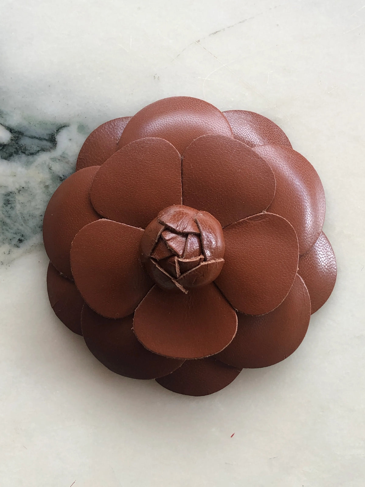 Broochella Men’s Leather Camelia Brooch in rich brown, a handmade designer leather flower brooch with layered sculptural petals and bud centre, photographed on white marble.