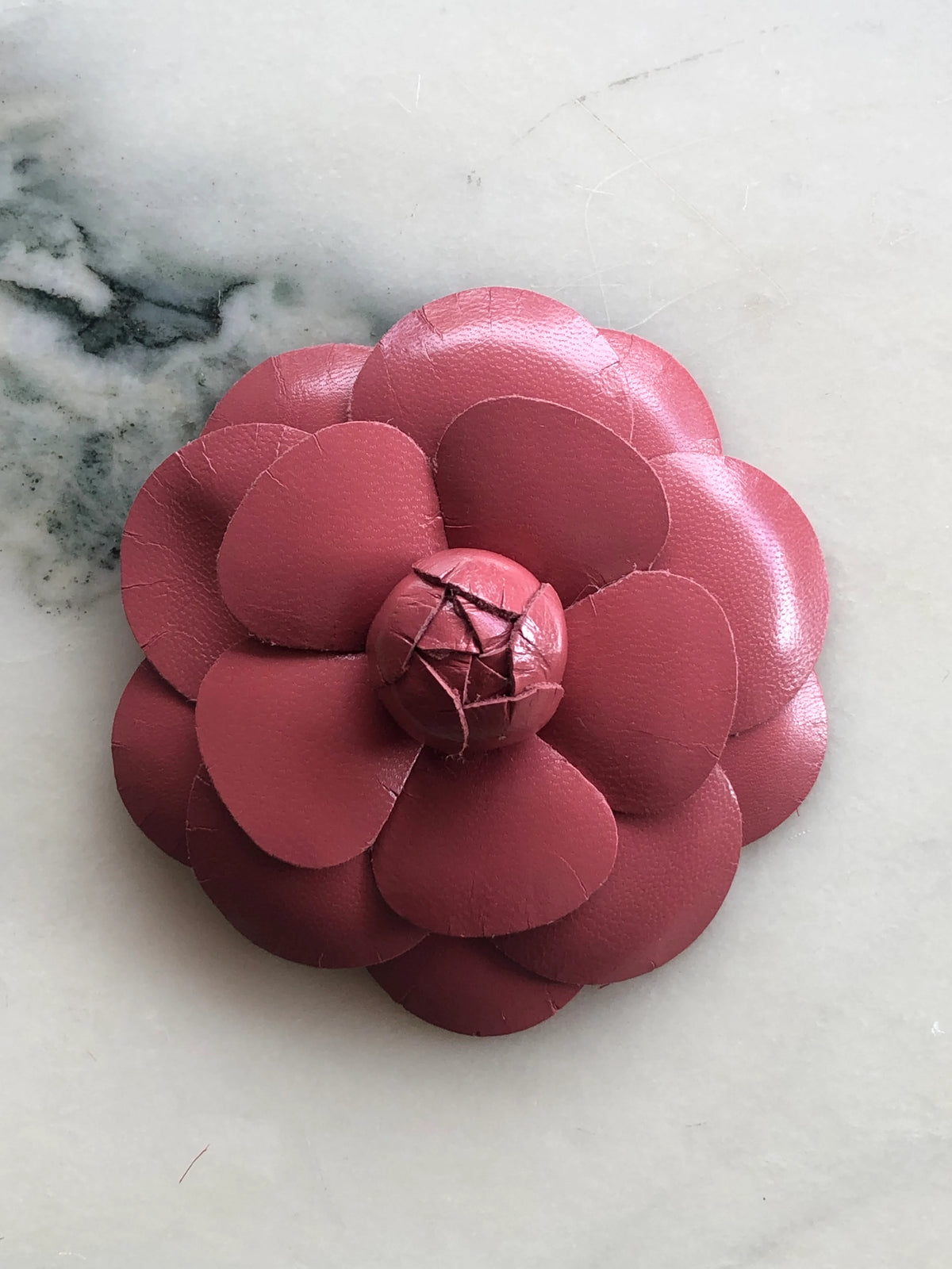Broochella Men’s Leather Camelia Brooch in rose gold, a handmade designer leather flower brooch with layered sculptural petals and bud centre, photographed on white marble.